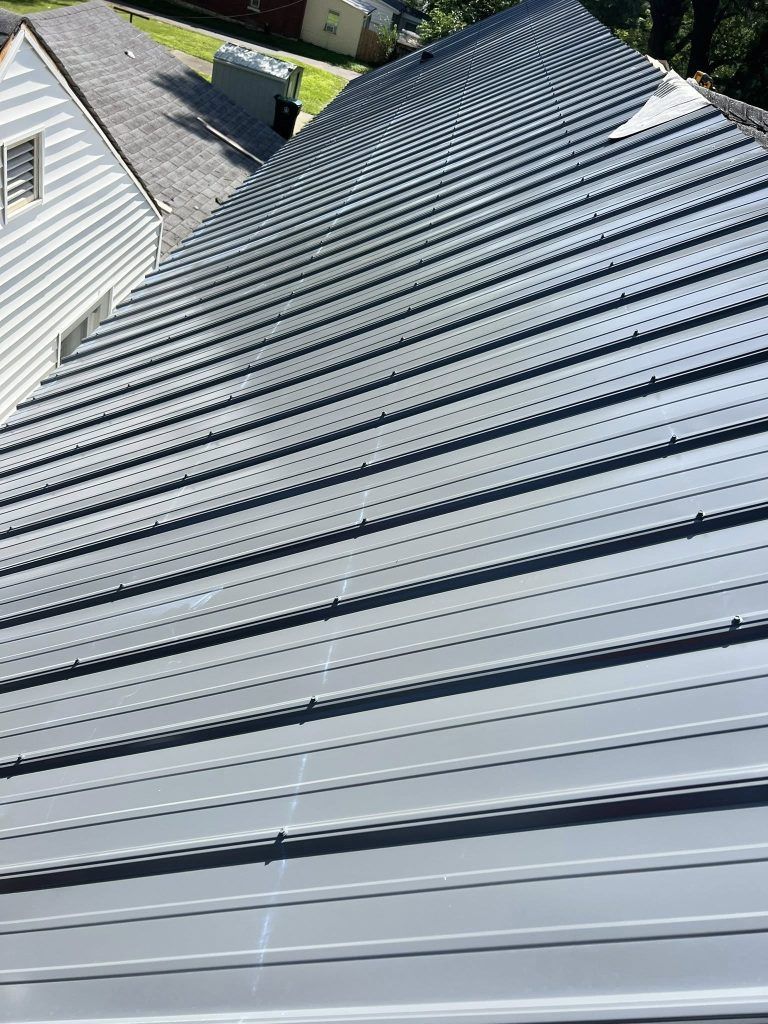 A high-angle view of a gray, ribbed metal roof on a residential home next to a white-sided building.