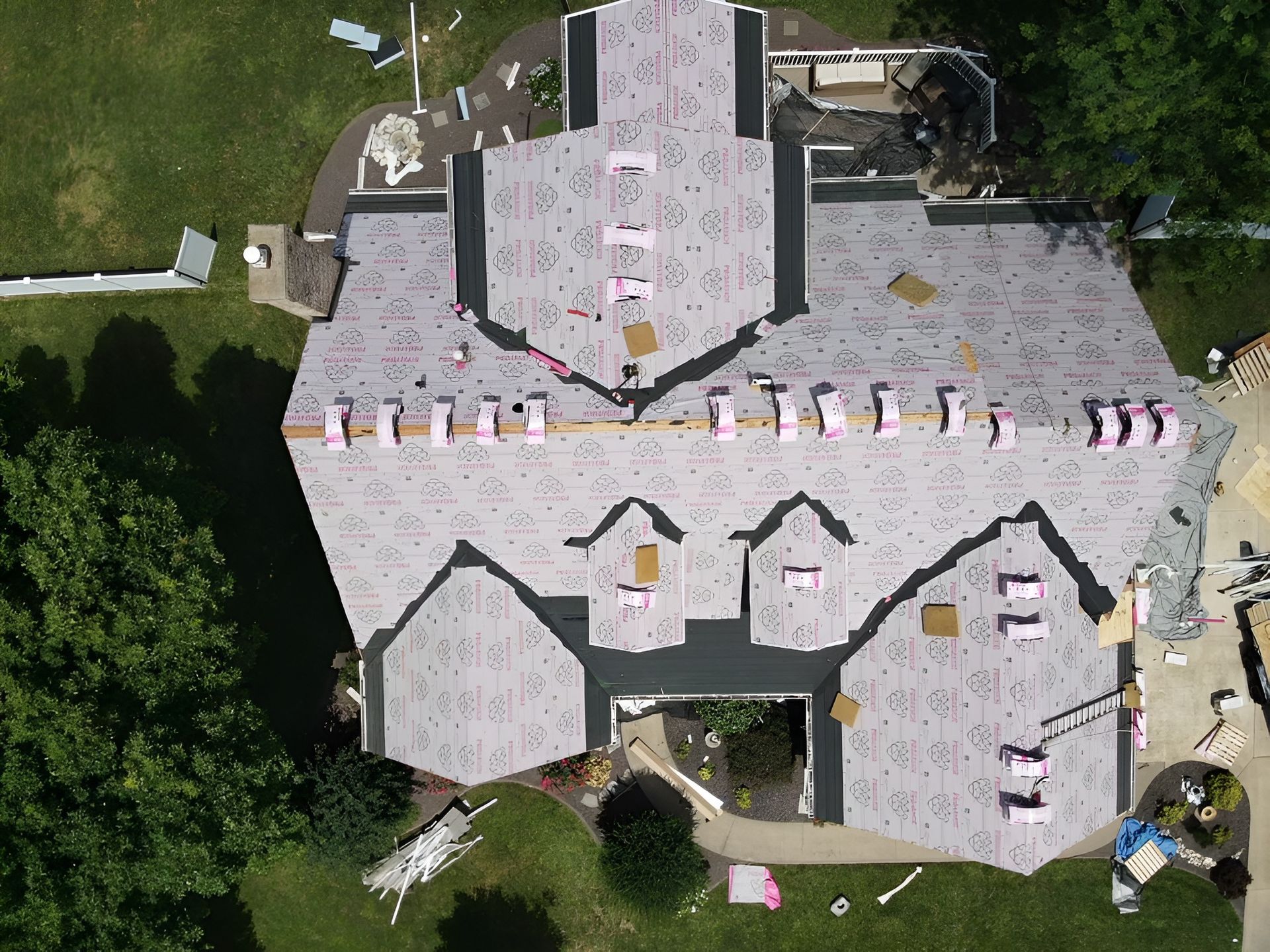 Aerial view of a residential house roof undergoing renovation with grey underlayment and bundles of roofing materials.
