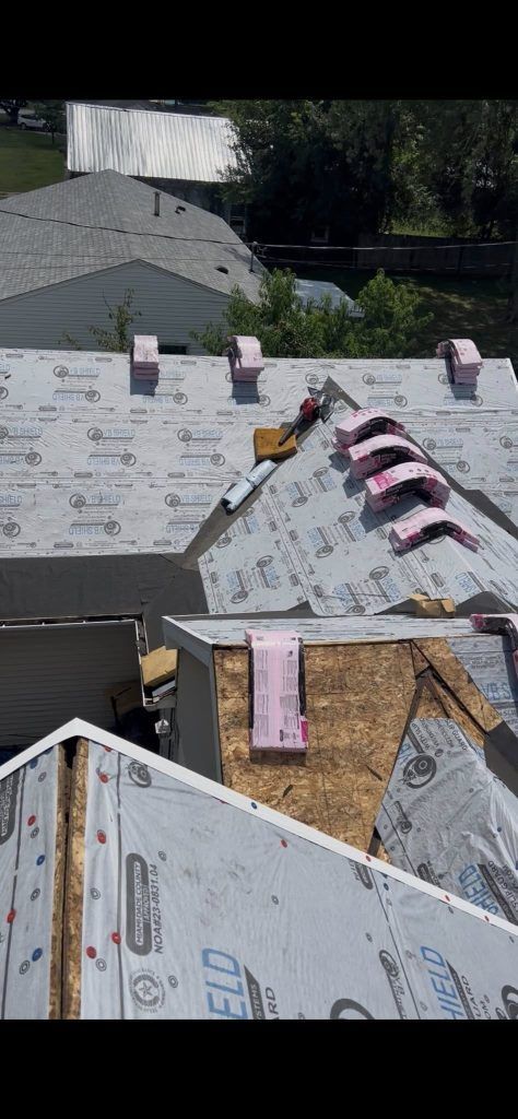 A roof under construction featuring white underlayment, pink foam board insulation pieces, and a partially exposed roof deck.