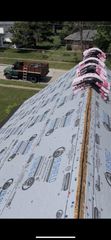 A roof under construction with gray underlayment and stacks of roofing shingles along the ridge, viewed from above.
