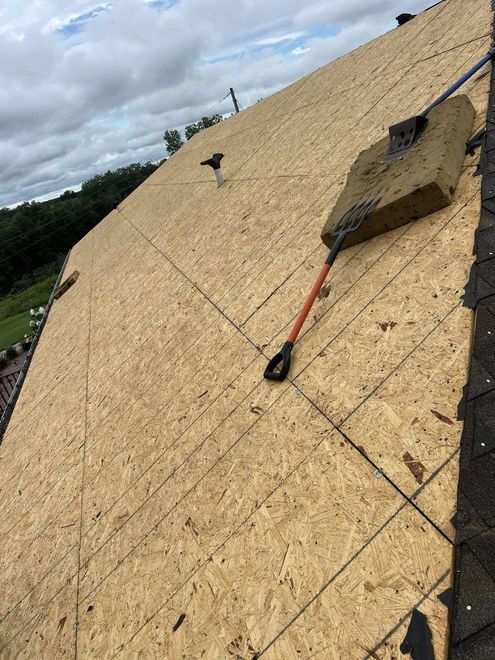 A roof undergoing renovation, with exposed plywood sheeting, a pitch fork tool, and a square of insulation material.
