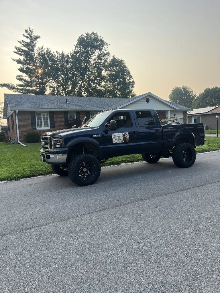 A lifted black pickup truck parked on a residential street in front of a brick house.