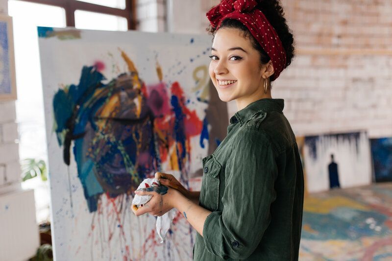 A young adult woman is standing in front of a painting on a canvas.