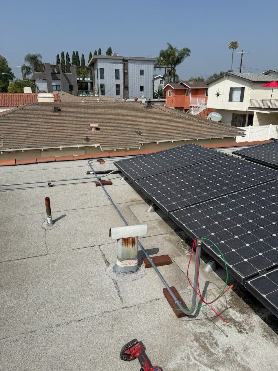 Rooftop solar panels installed on a flat roof with neighboring houses in the background.