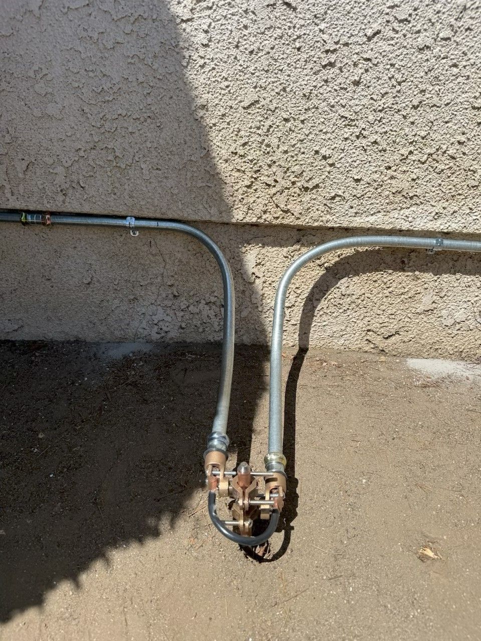 Two metal water pipes and valves against a rough stucco wall, with one pipe bent toward the ground.