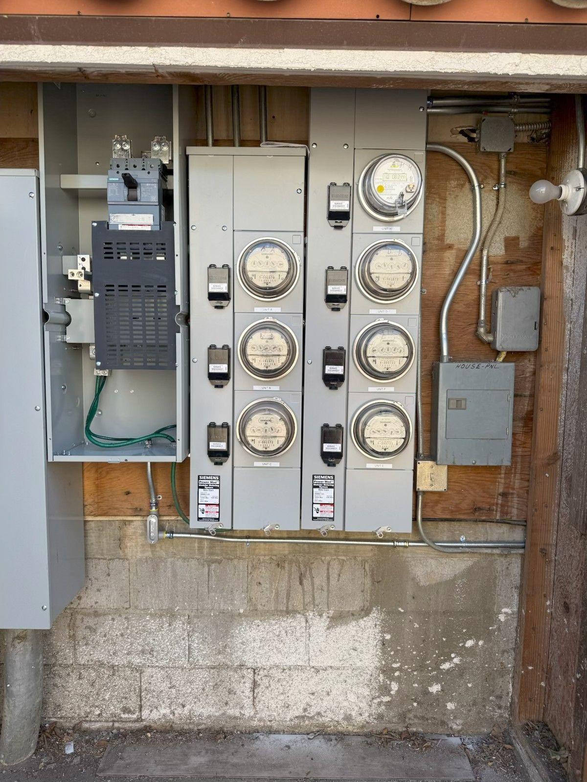 Electrical meter and breaker panels mounted on a weathered exterior wall under an overhang
