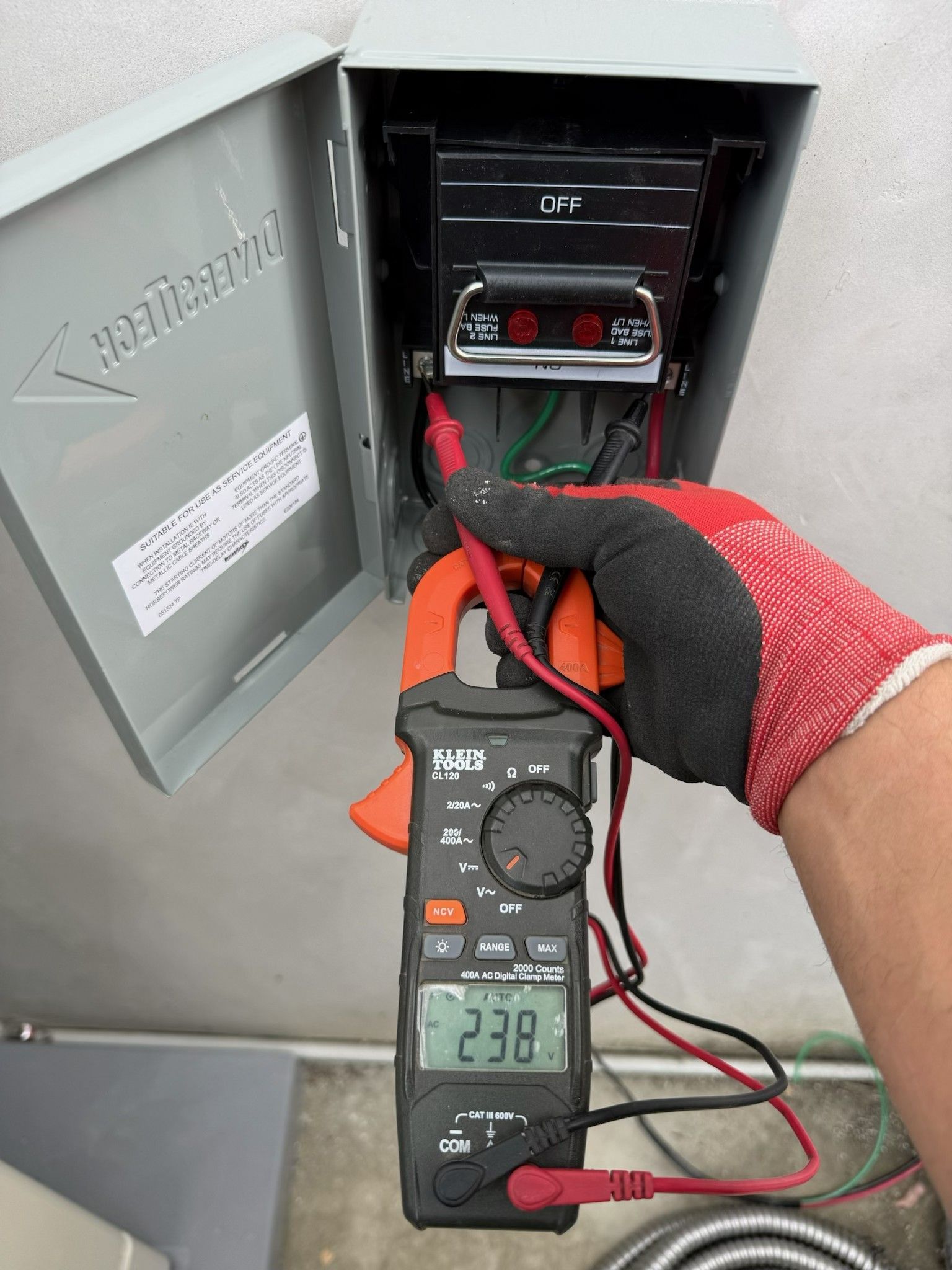 Gloved hand using a multimeter to test wiring inside an open electrical panel
