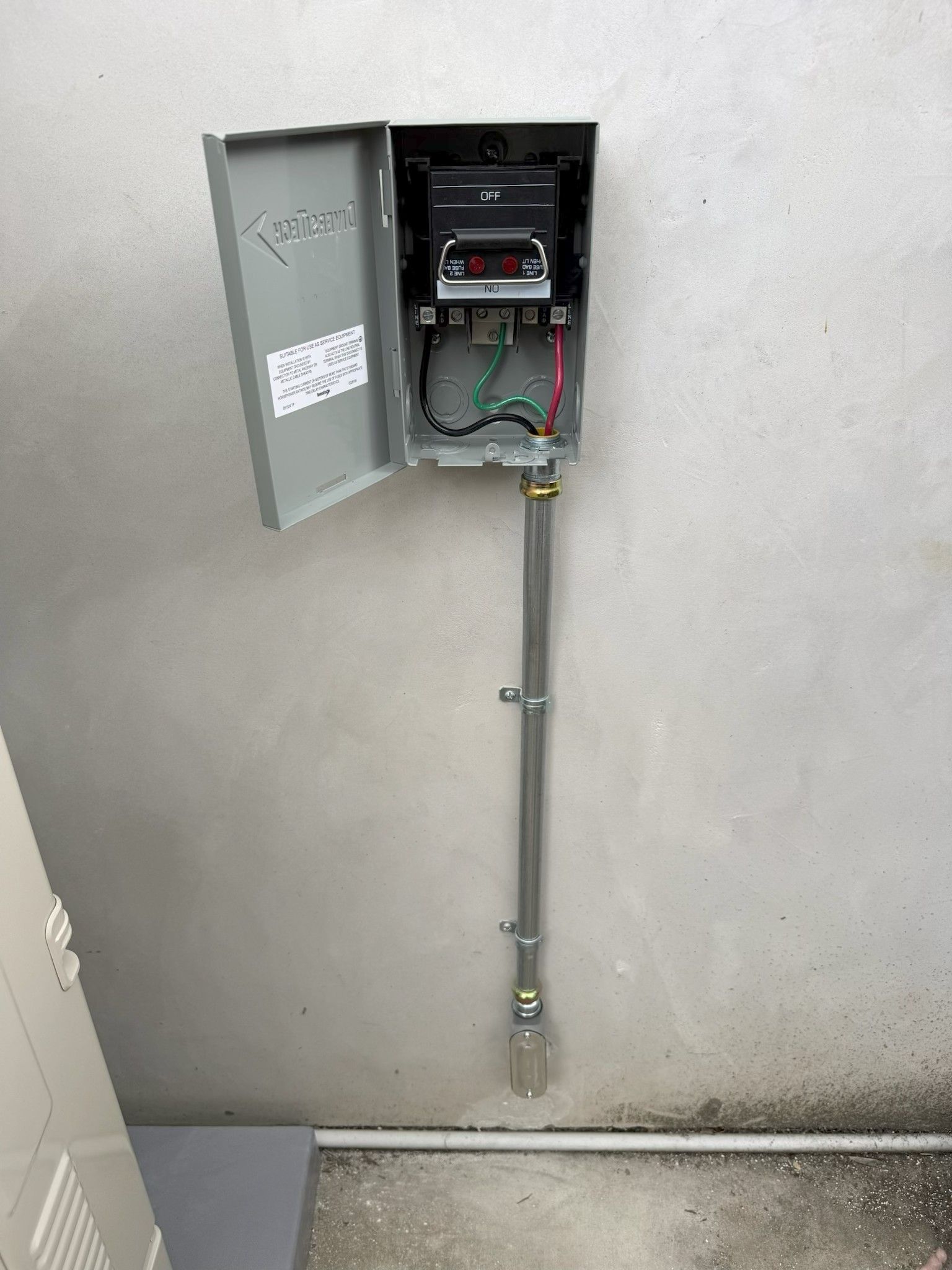 Open electrical meter panel with conduit mounted on a gray wall inside a room.