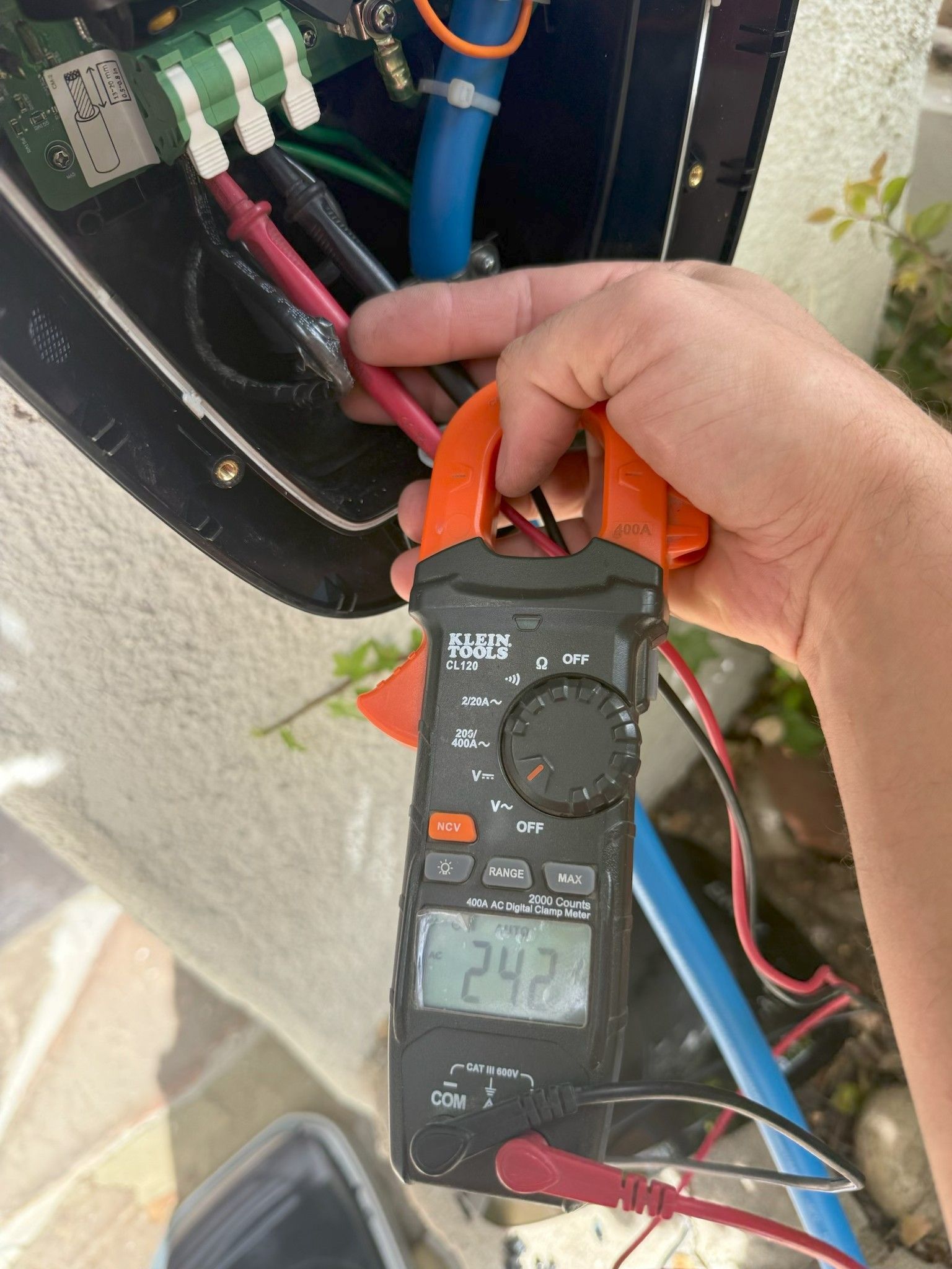 Hand holding a digital multimeter measuring wires inside an electrical panel