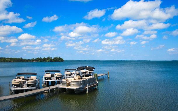 Three pontoon boats are docked at a dock on a lake.