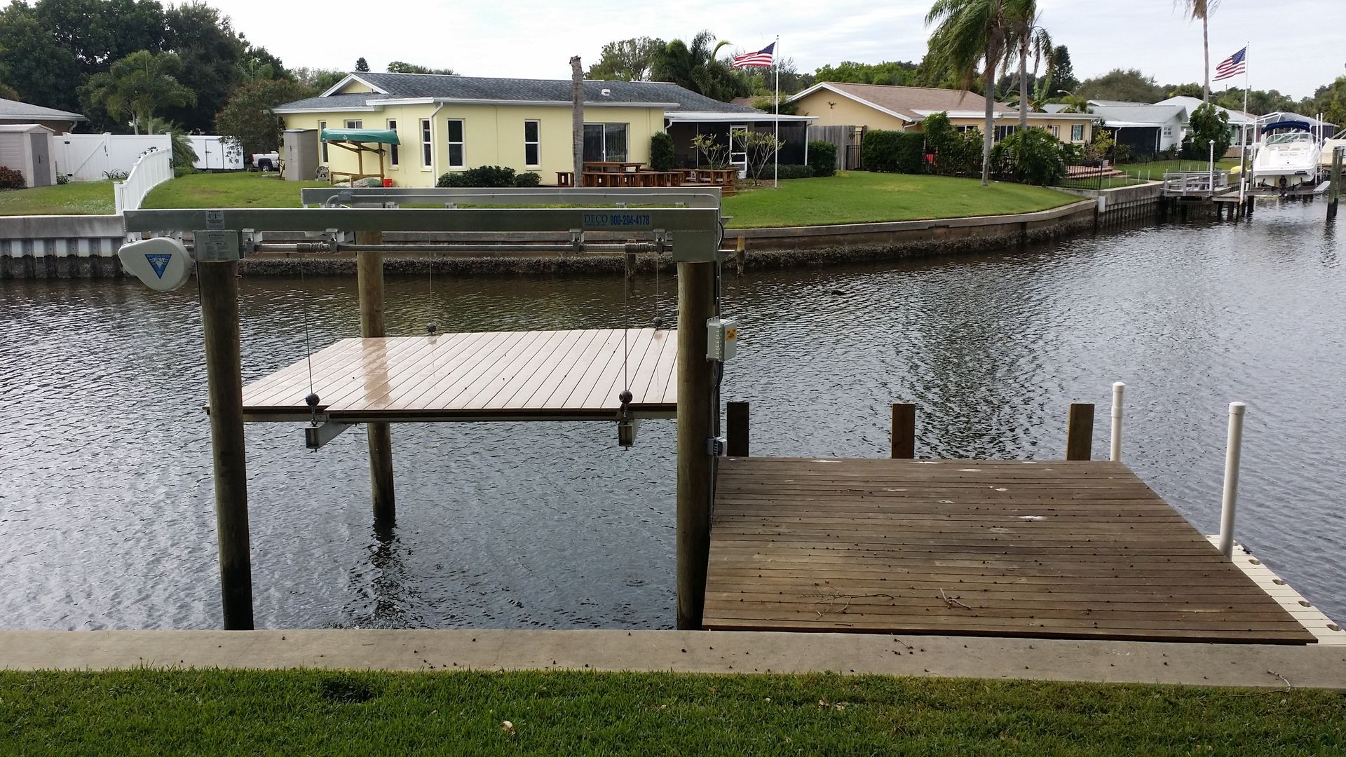 A dock in the middle of a body of water with a residential home in the background.