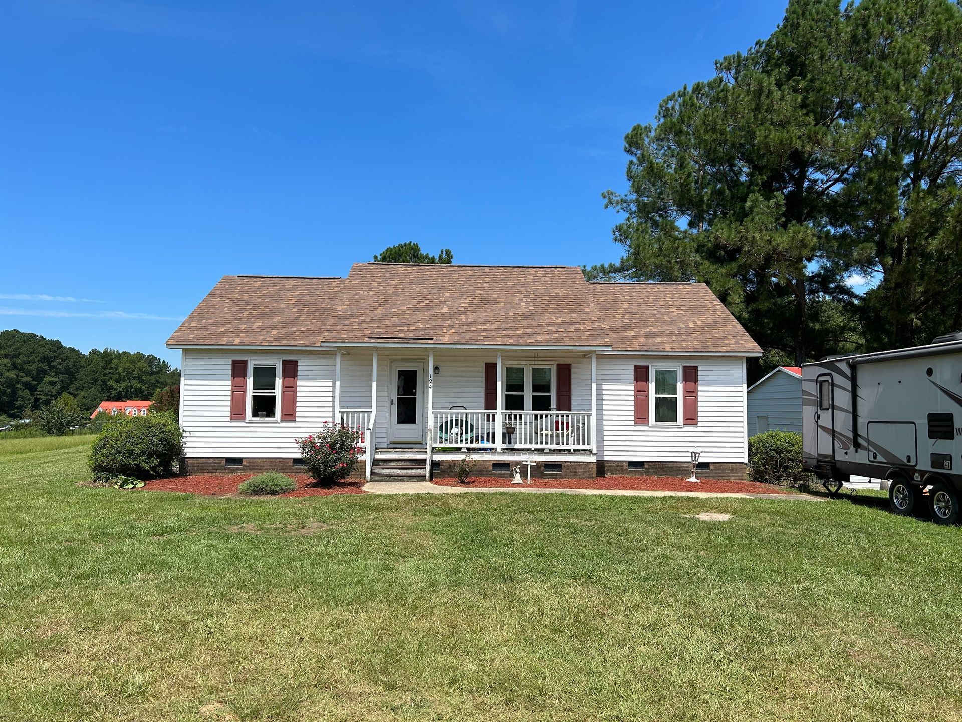 A white house with a porch and a trailer parked in front of it.