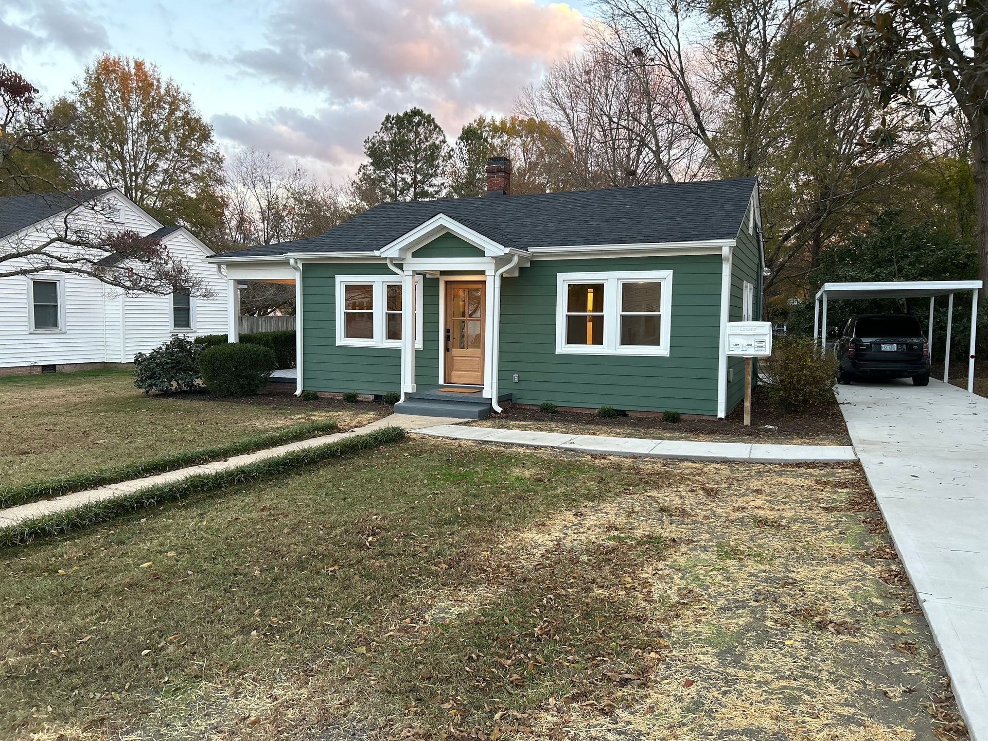 A small green house with a carport in front of it.