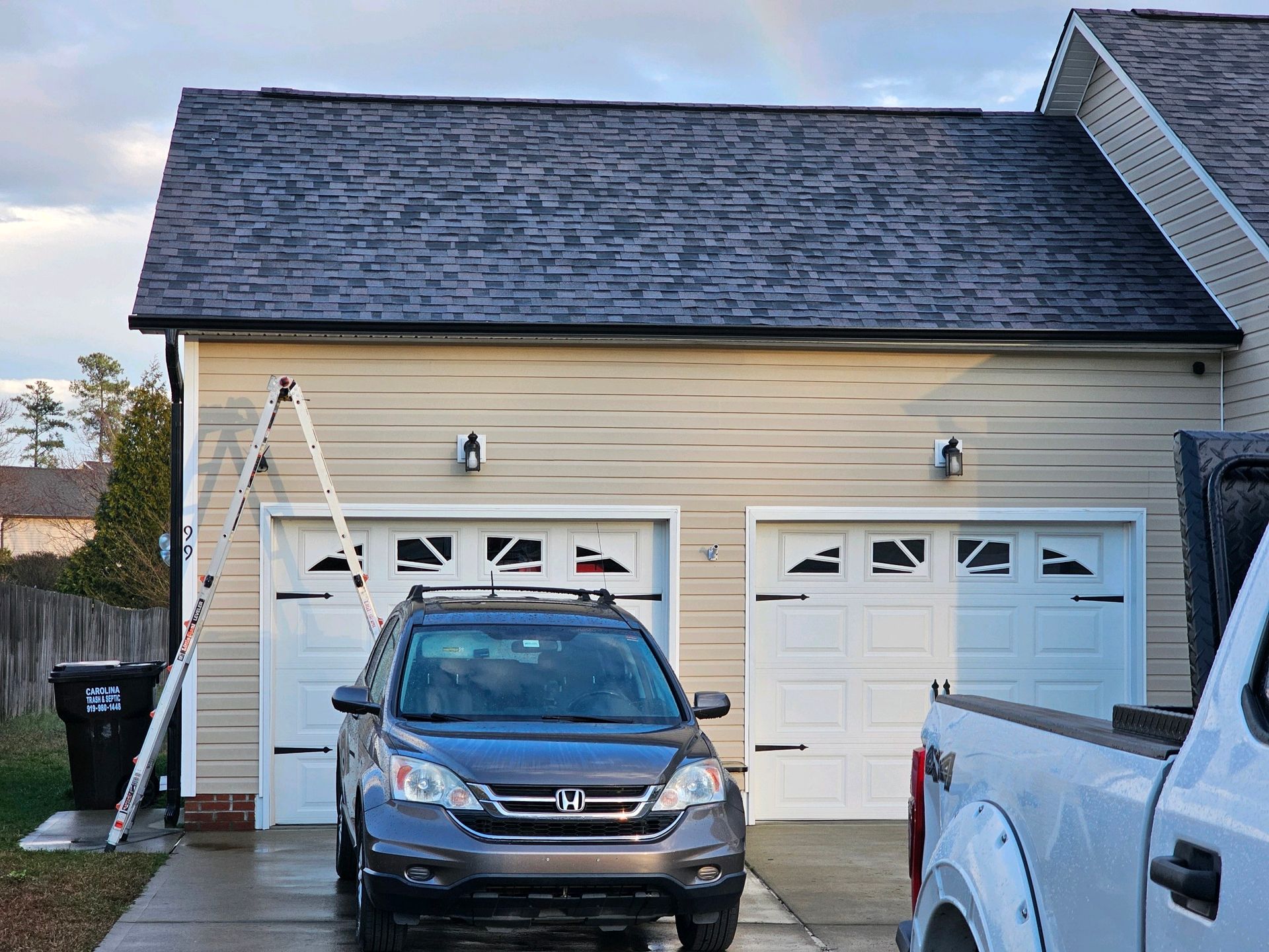 A car is parked in front of a garage next to a truck.