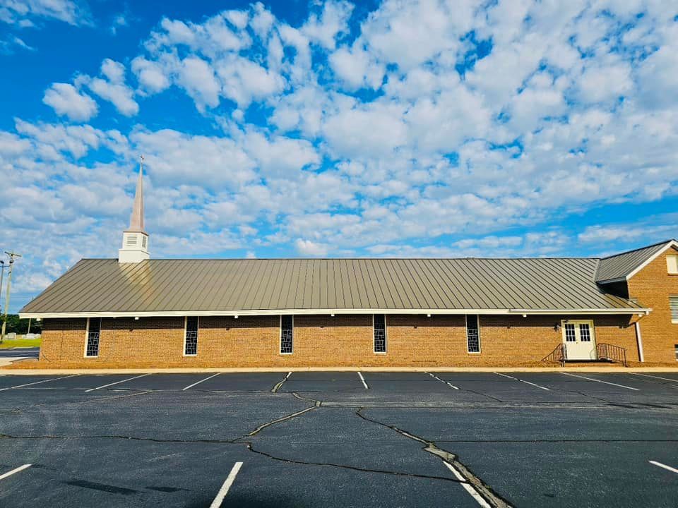 A church with a steeple and a parking lot in front of it.