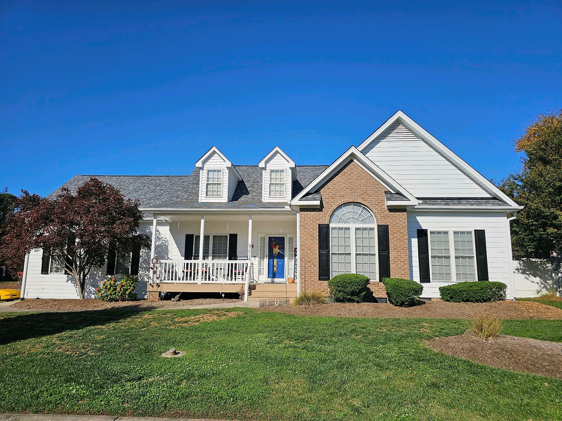 A large white and brick house with a large lawn in front of it.