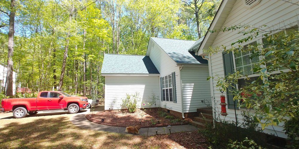 A red truck is parked in front of a white house.