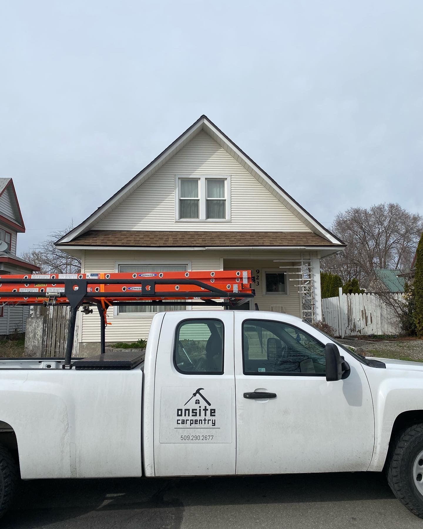 White pickup truck with ladder parked in front of a small, white house with a gabled roof.