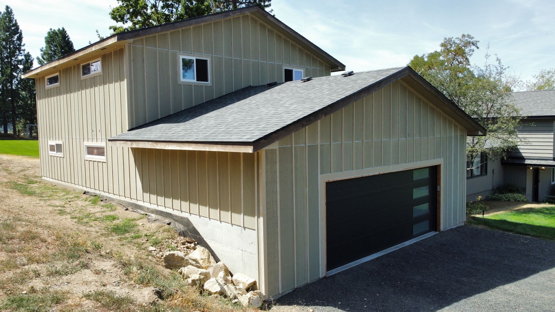 Two-story house with tan siding, black garage door, and a gravel driveway.
