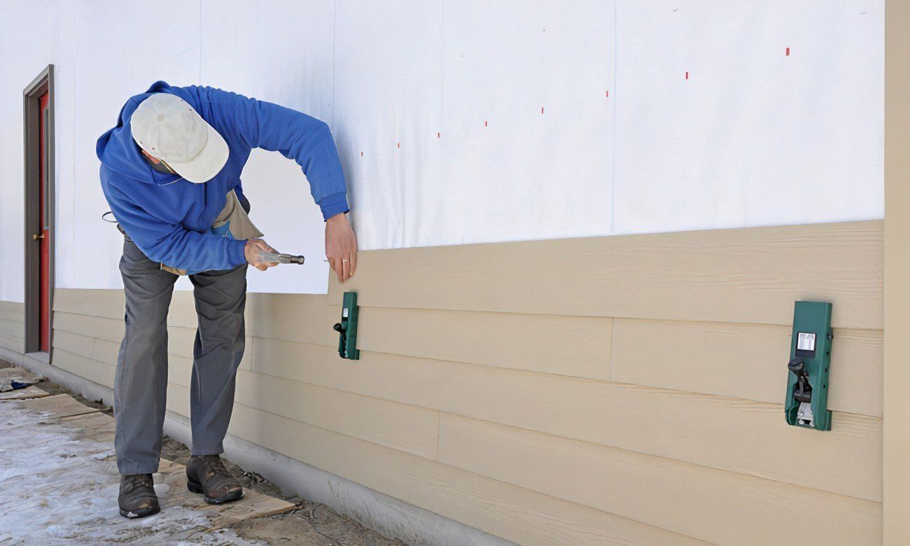 Person installs siding on a wall using green clips and a hammer.