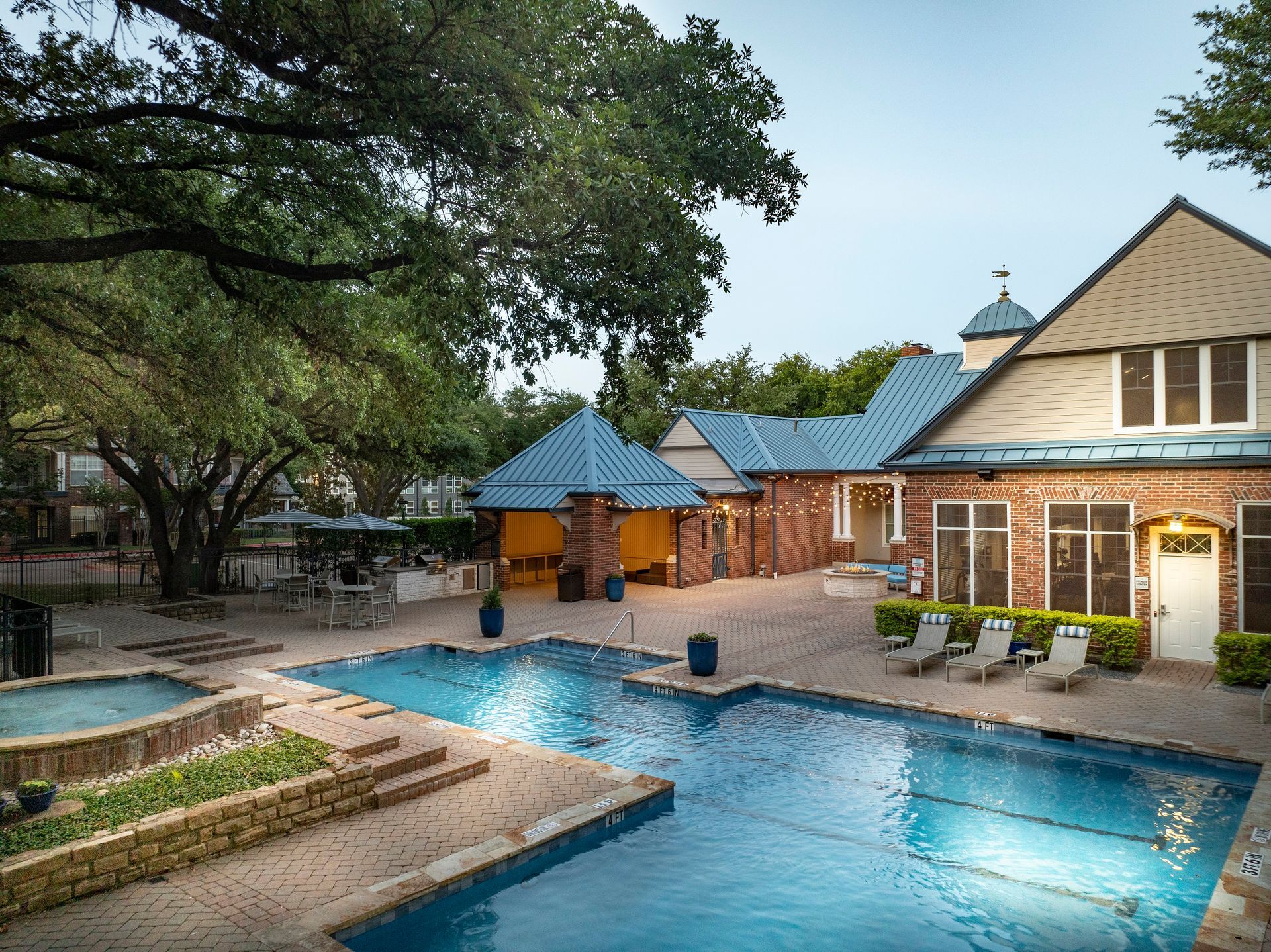 A pool area with two pools, brick buildings, and a gazebo under a cloudy sky at Townhomes of Bent Tree, offers Far North Dallas apartments for rent with garages.