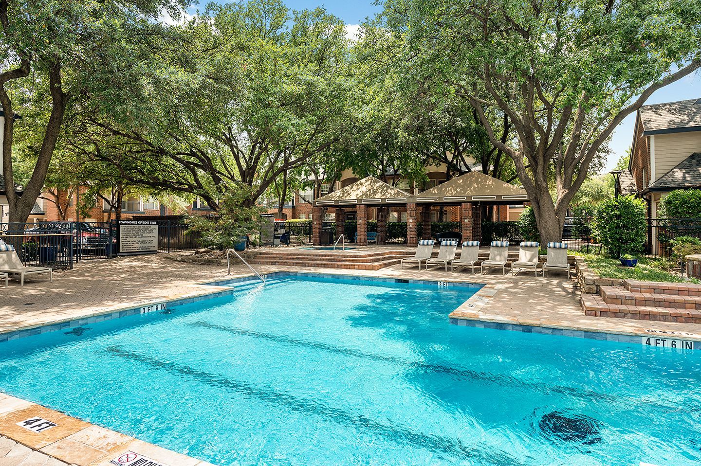 Swimming pool with turquoise water, lounge chairs, and a shaded seating area at Townhomes of Bent Tree, offers North Dallas apartments for rent.