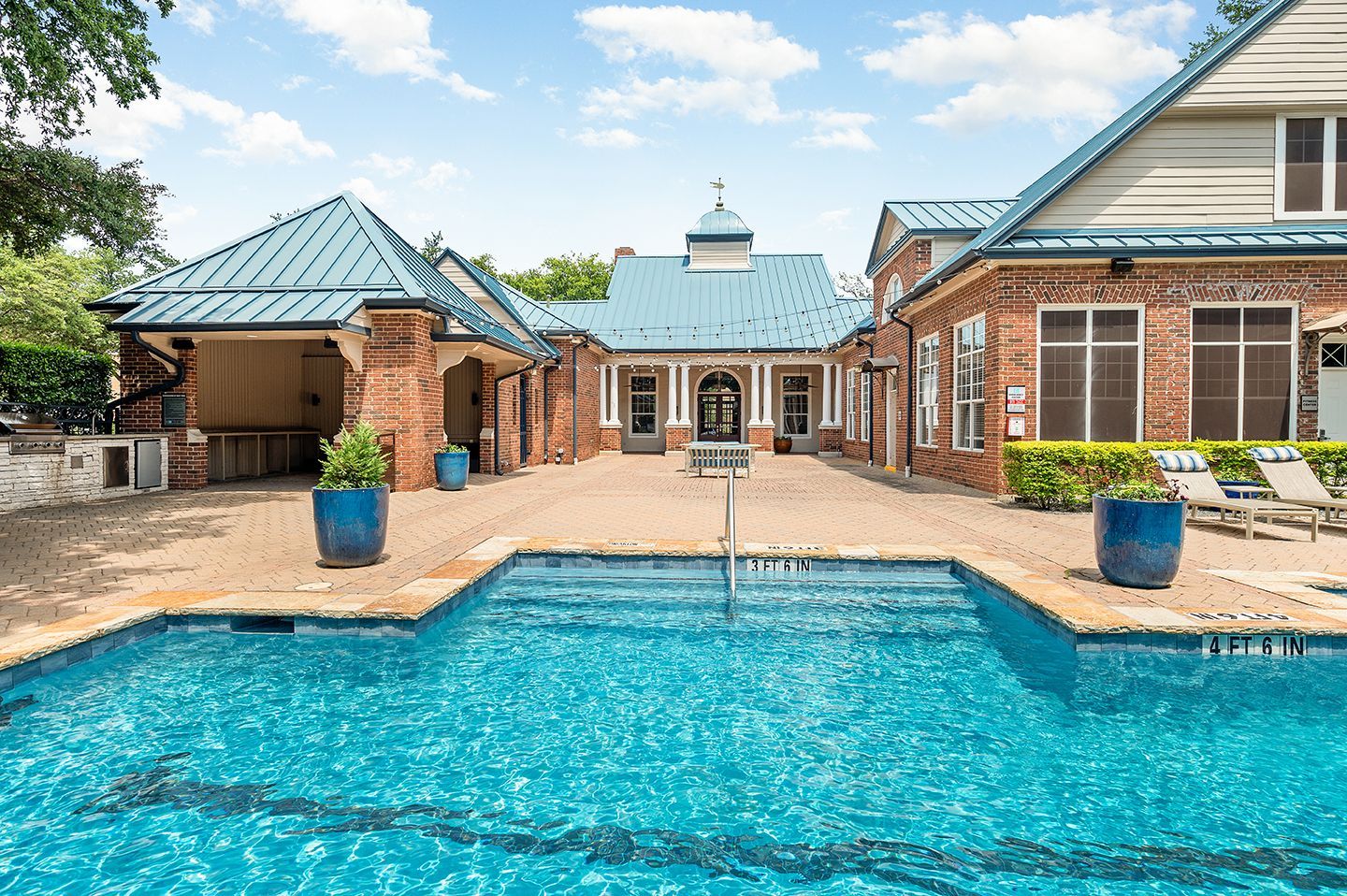Pool with building in the background; blue roof, brick exterior, and blue planters.
