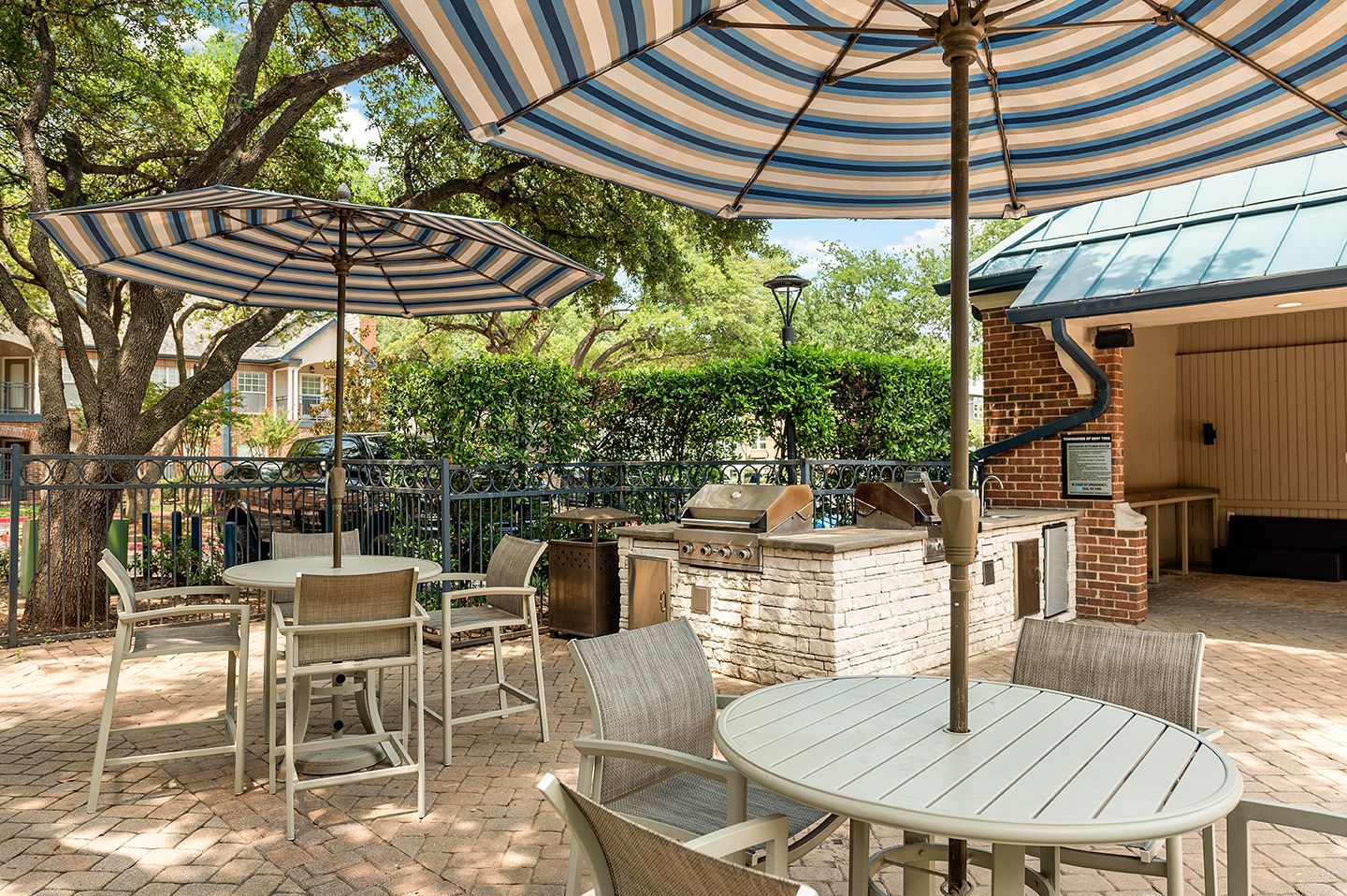 Outdoor patio with tables, chairs, umbrellas, and a brick grilling area at Townhomes of Bent Tree, offers pet-friendly apartments in Plano ISD.