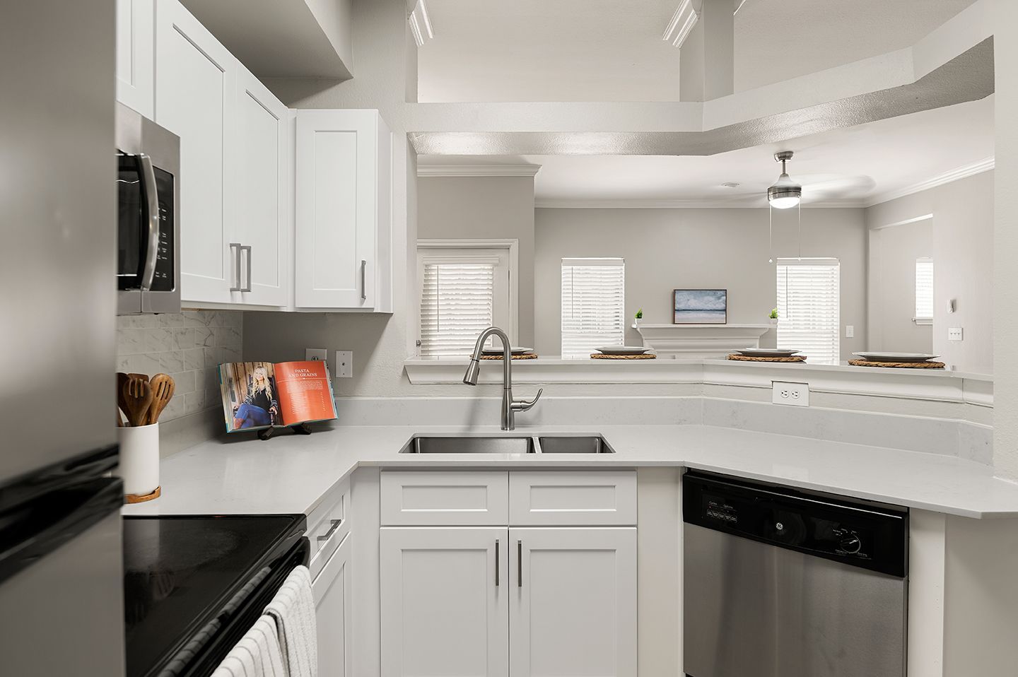 White kitchen with quartz countertops, stainless steel appliances, and a view of a living area at Townhomes of Bent Tree, offers apartments in North Dallas, TX.