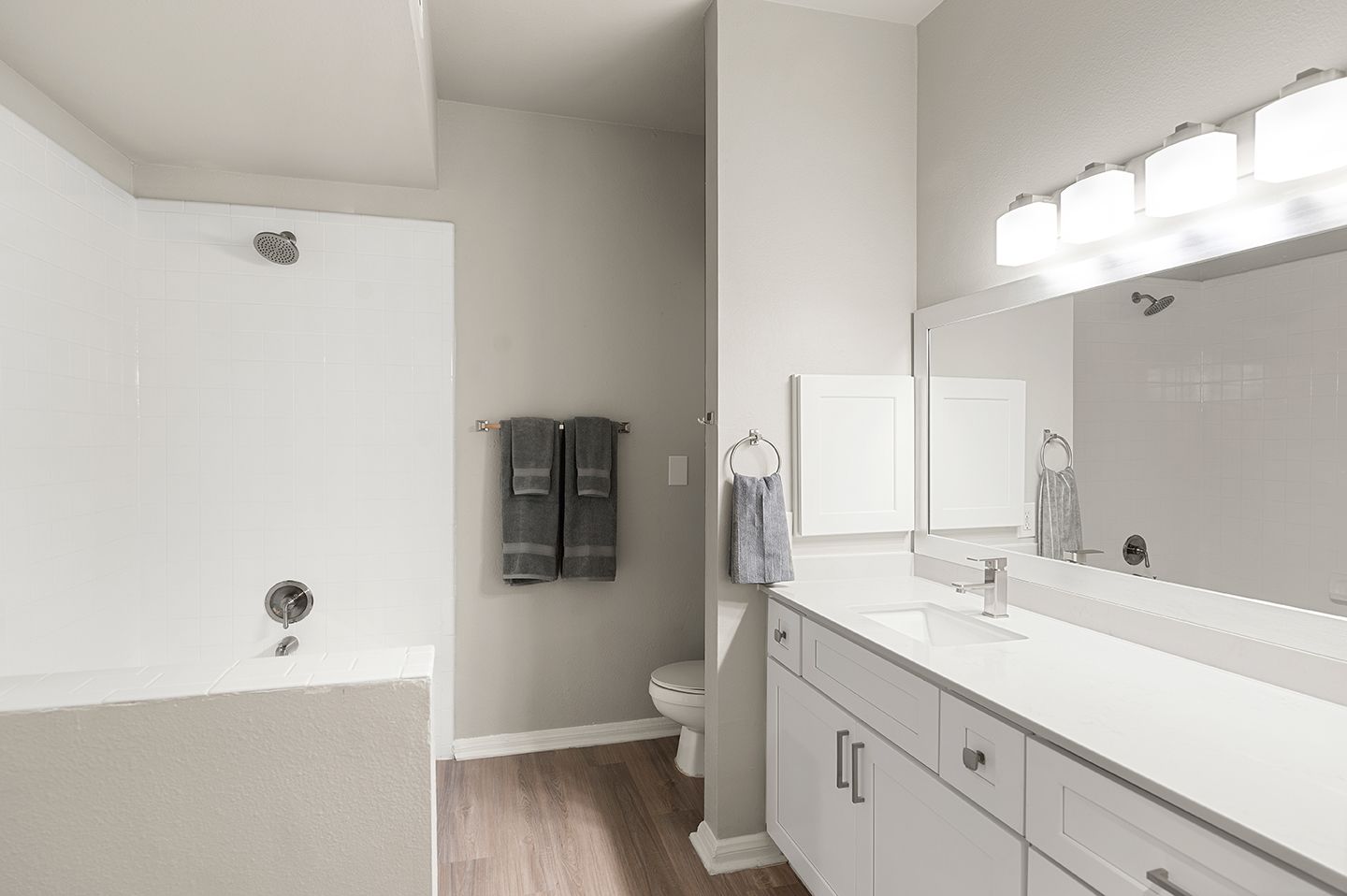 Modern bathroom with white cabinets, a long mirror, shower, and gray towels at Townhomes of Bent Tree, offers apartments for rent in Dallas, TX.