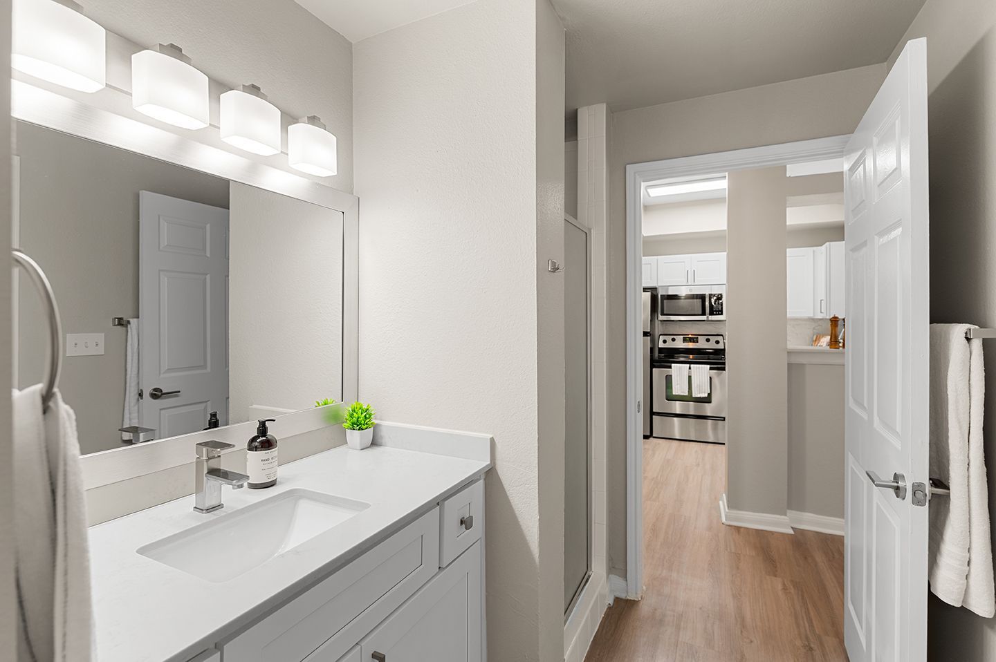 Bathroom with a sink, mirror, and open doorway to the kitchen at Townhomes of Bent Tree, offers apartments for rent in Far North Dallas, TX. White cabinetry and walls.