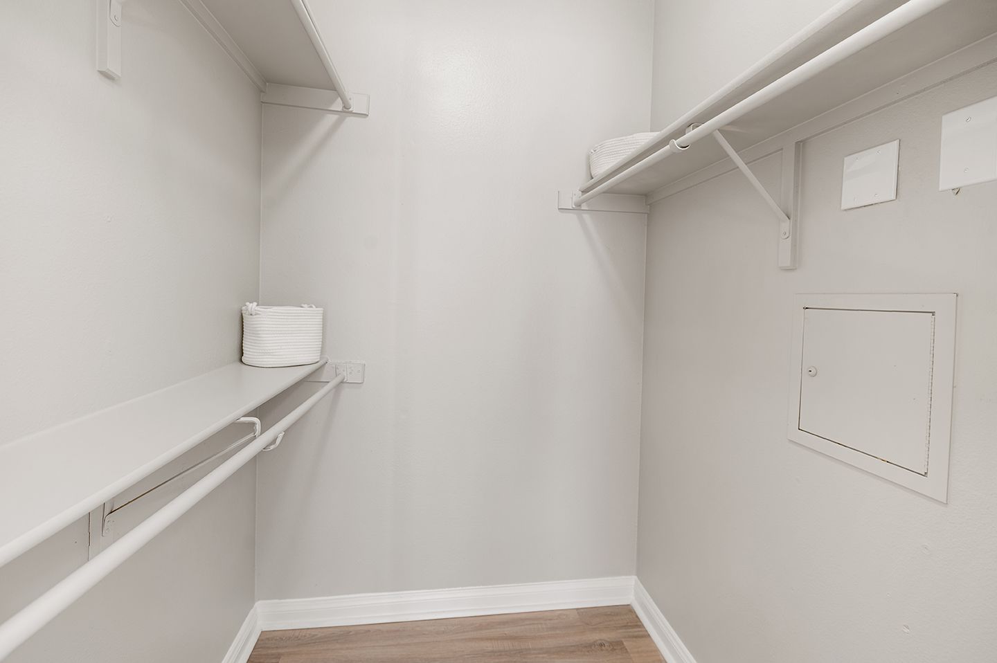 Empty walk-in closet with white shelves and rod, light gray walls, and wood-look flooring at Townhomes of Bent Tree, offers apartments for rent in Far North Dallas, TX.