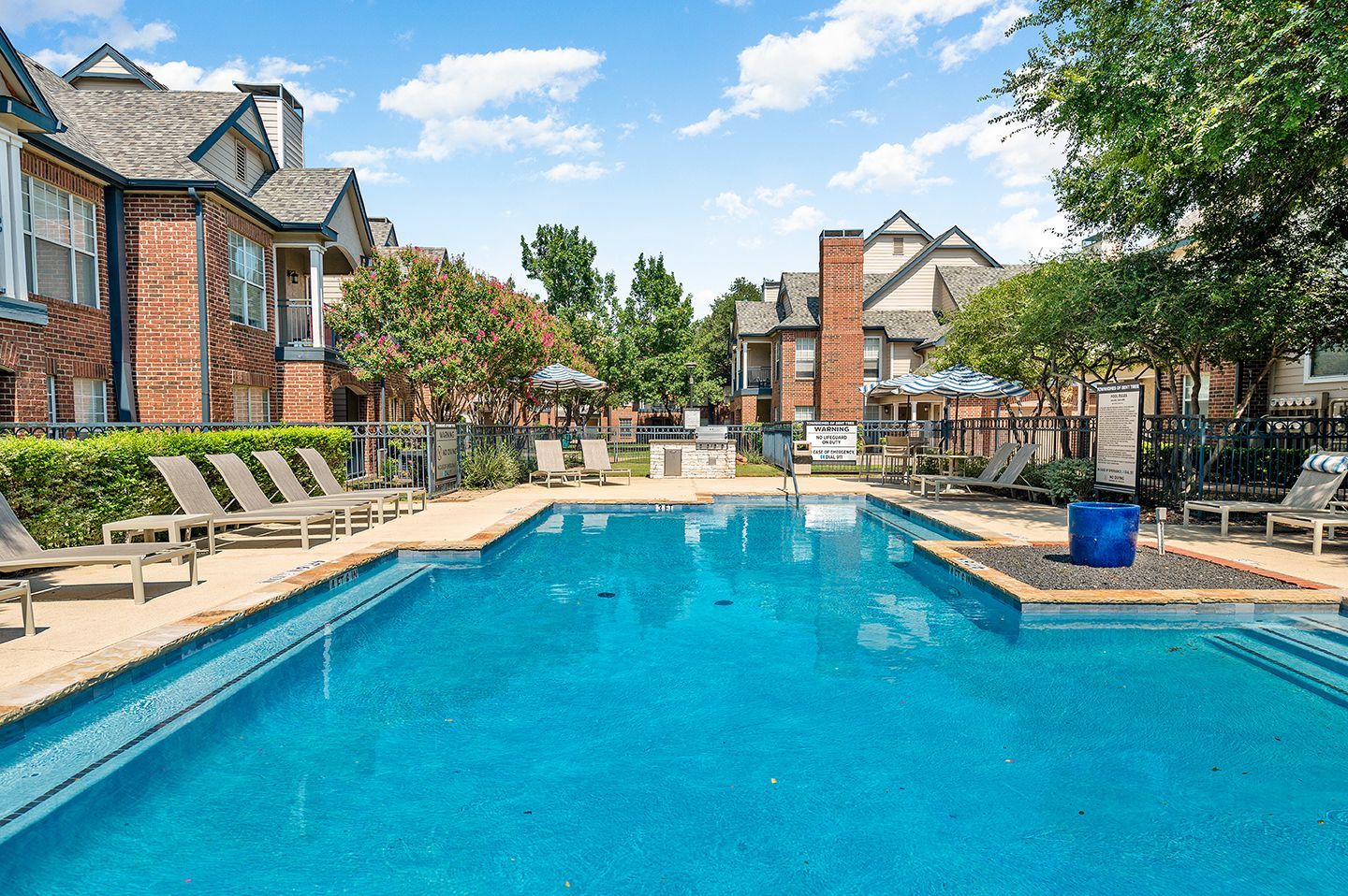 Swimming pool at apartment complex with lounge chairs, blue water, and brick buildings at Townhomes of Bent Tree, offers North Dallas apartments for rent with garages.