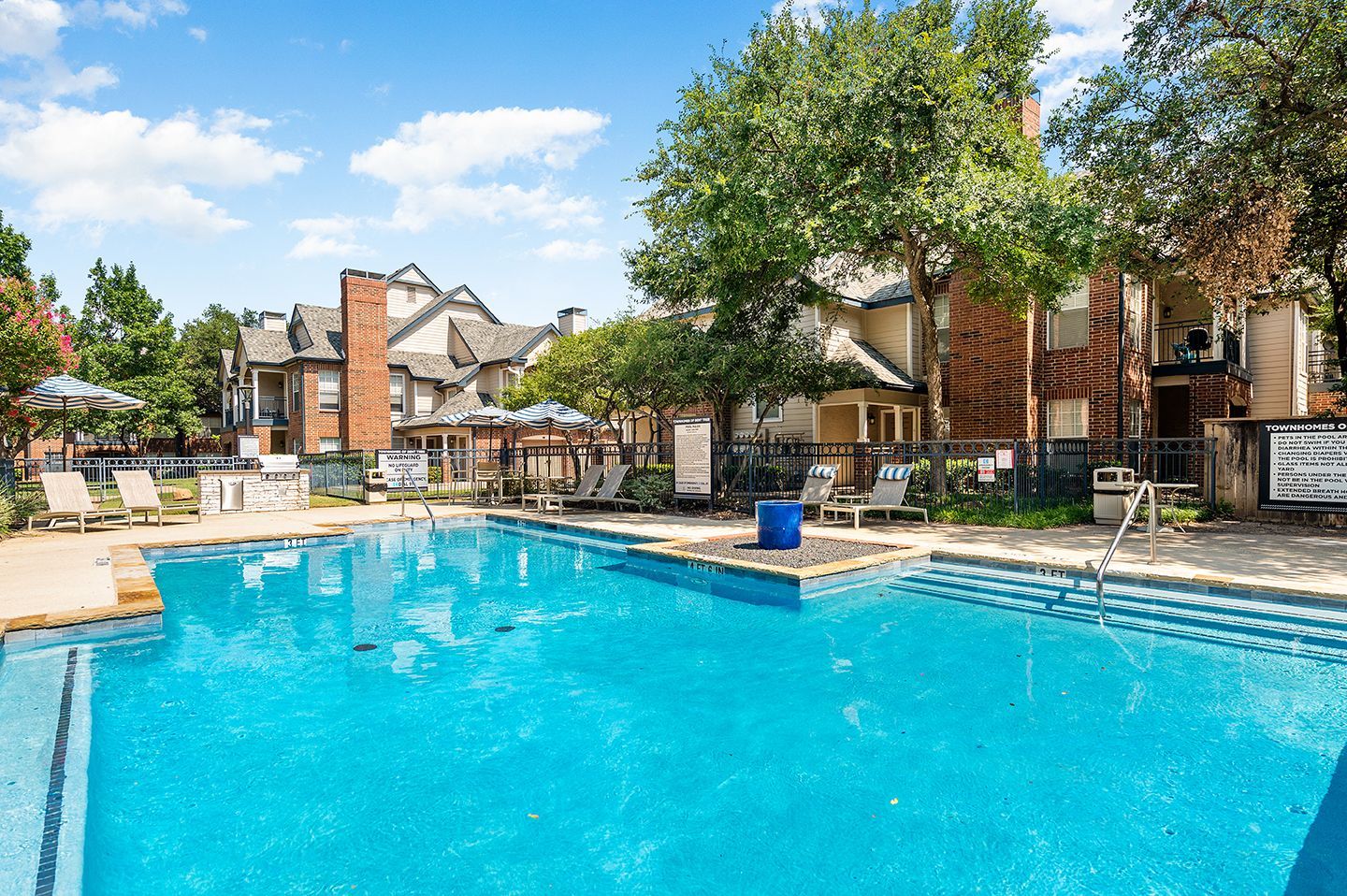 Swimming pool at an apartment complex with lounge chairs and trees under a blue sky at Townhomes of Bent Tree, offers North Dallas apartments for rent with garages.
