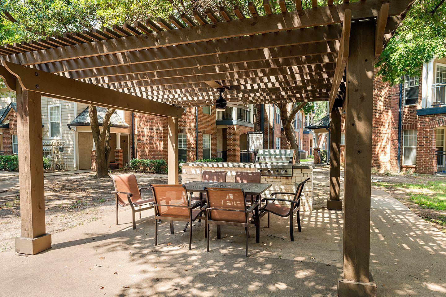 Outdoor dining area with wooden pergola, table, chairs, and brick buildings.