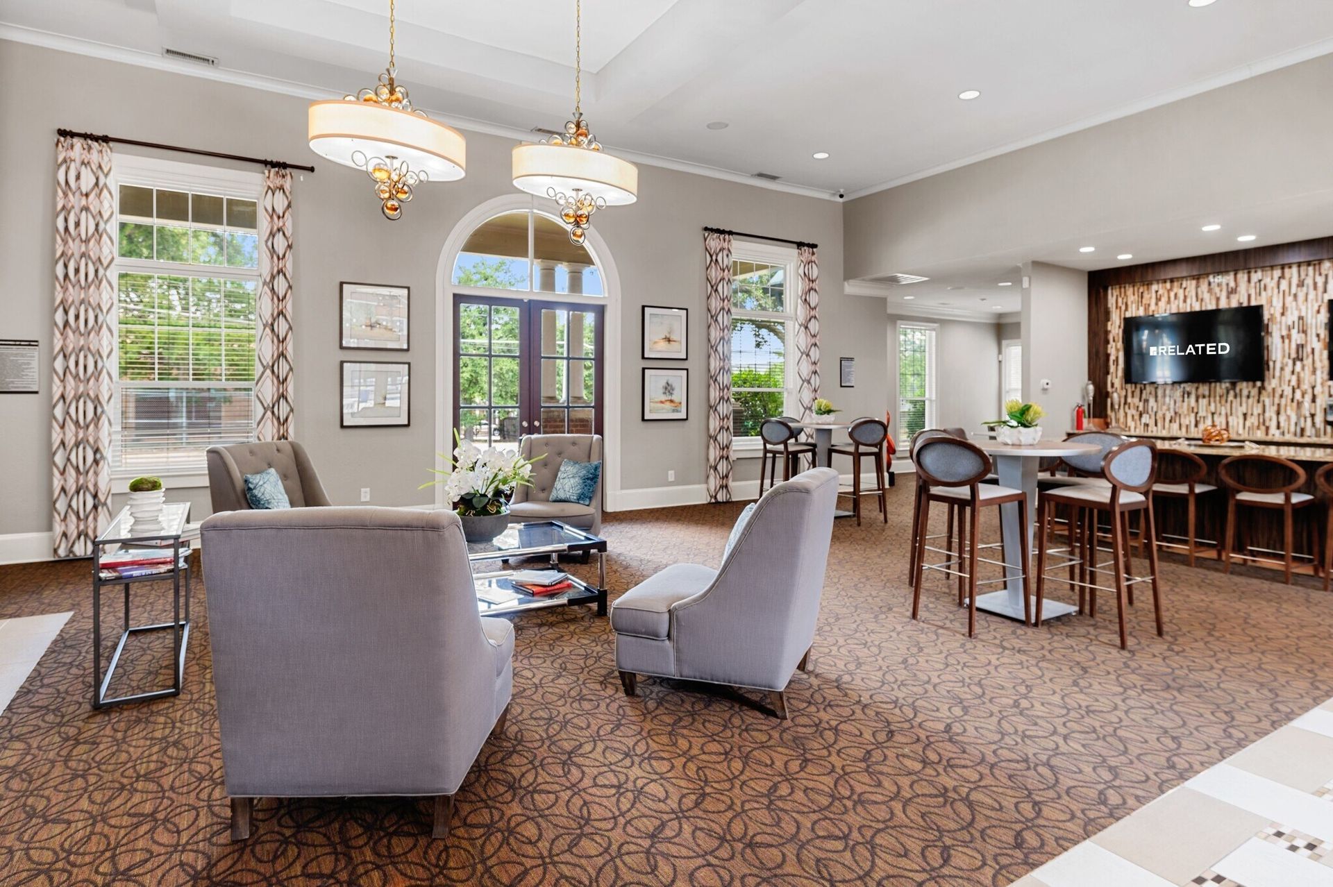A cozy lounge area with seating, high-top tables, and a bar, under ornate chandeliers at Townhomes of Bent Tree, offers apartments in Dallas, TX.