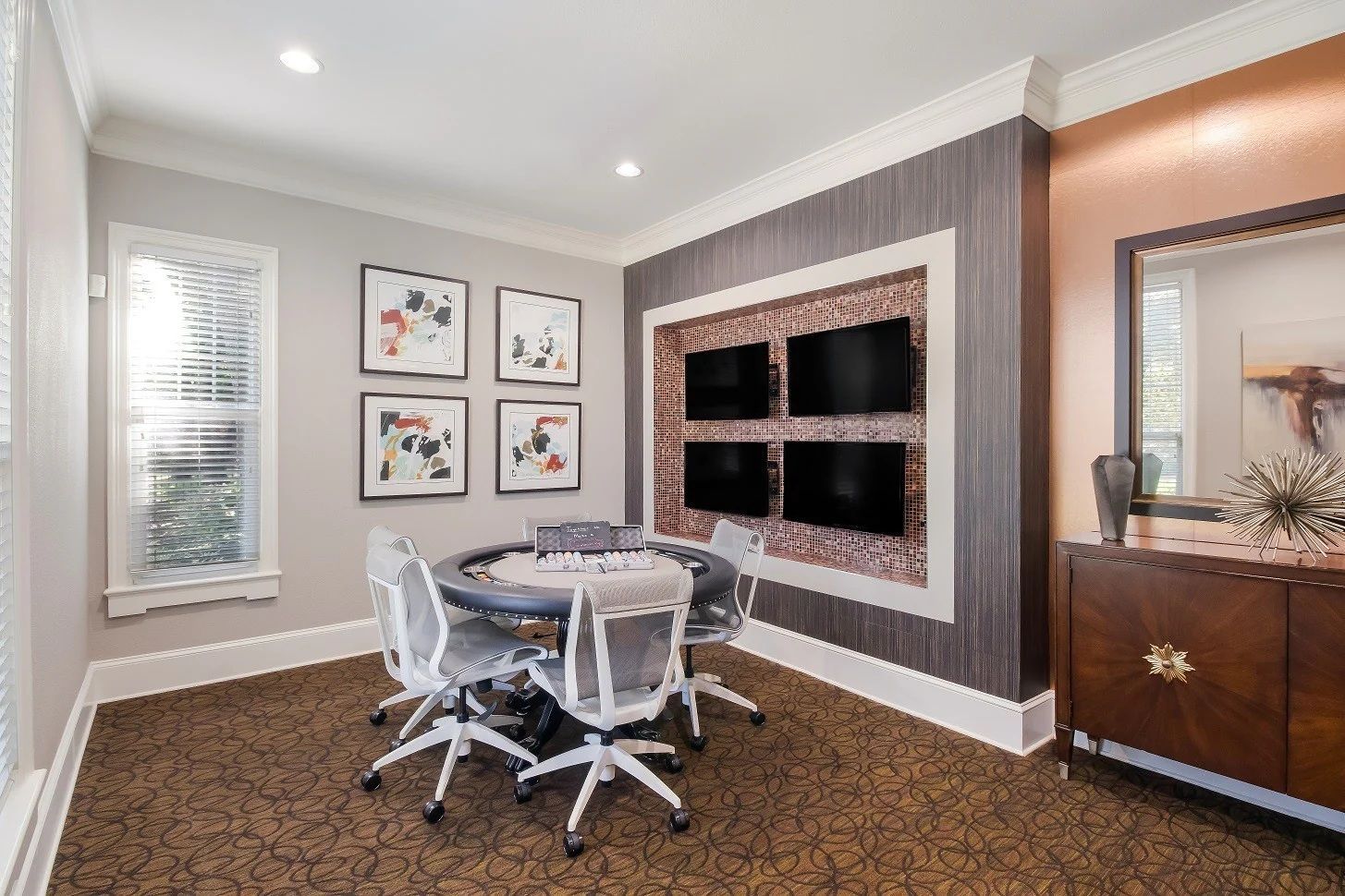 Gaming room with poker table, four TVs, and artwork at Townhomes of Bent Tree, offers apartments in Dallas, TX. White chairs, brown carpet.