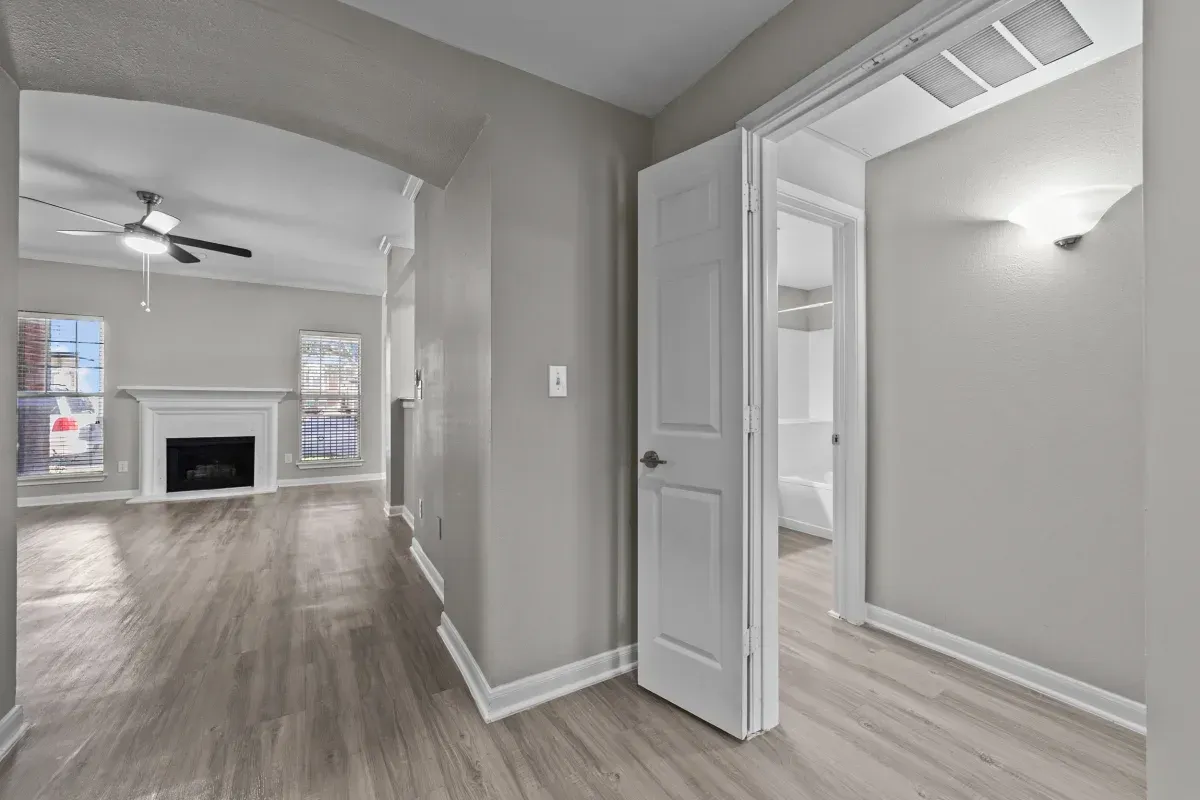 Hallway with light gray walls, white trim, and a view into a living room with a fireplace at Townhomes of Bent Tree, offers apartments in North Dallas, TX.