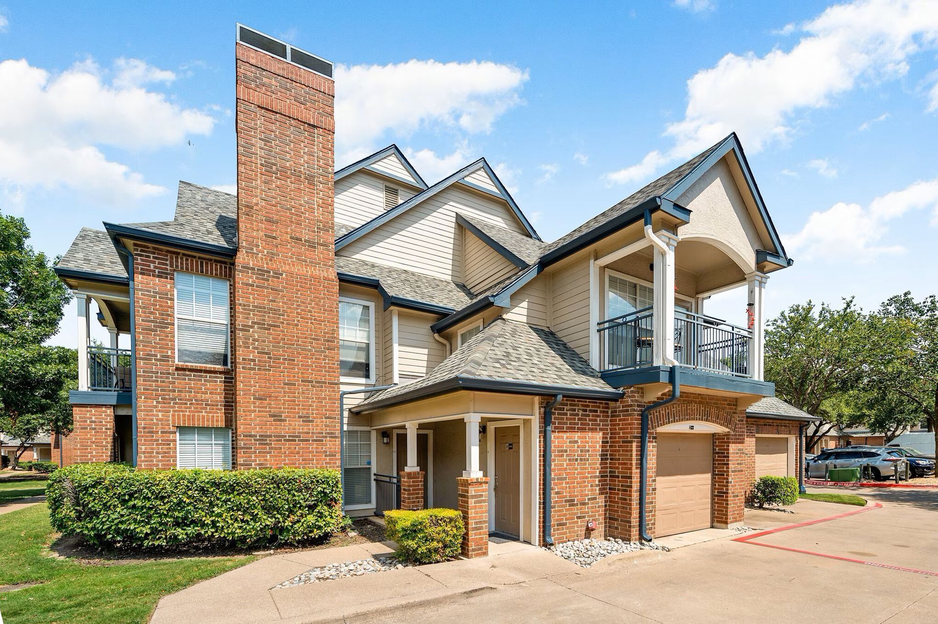 Multi-story brick and beige townhome with a chimney and balconies, on a sunny day at Townhomes of Bent Tree, offers North Dallas apartments for rent with garages.