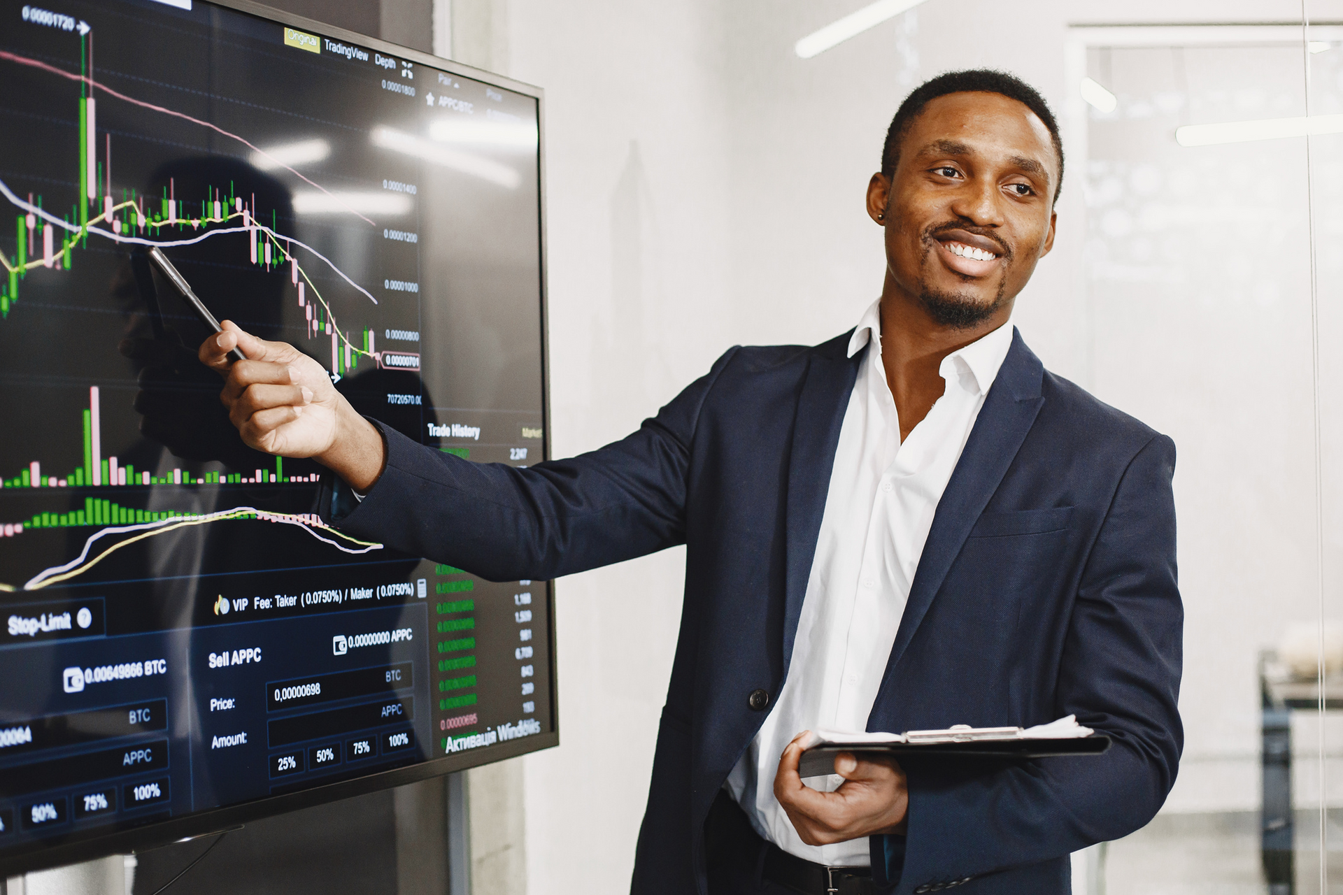 Man in suit points at a financial graph on a large screen, smiling.