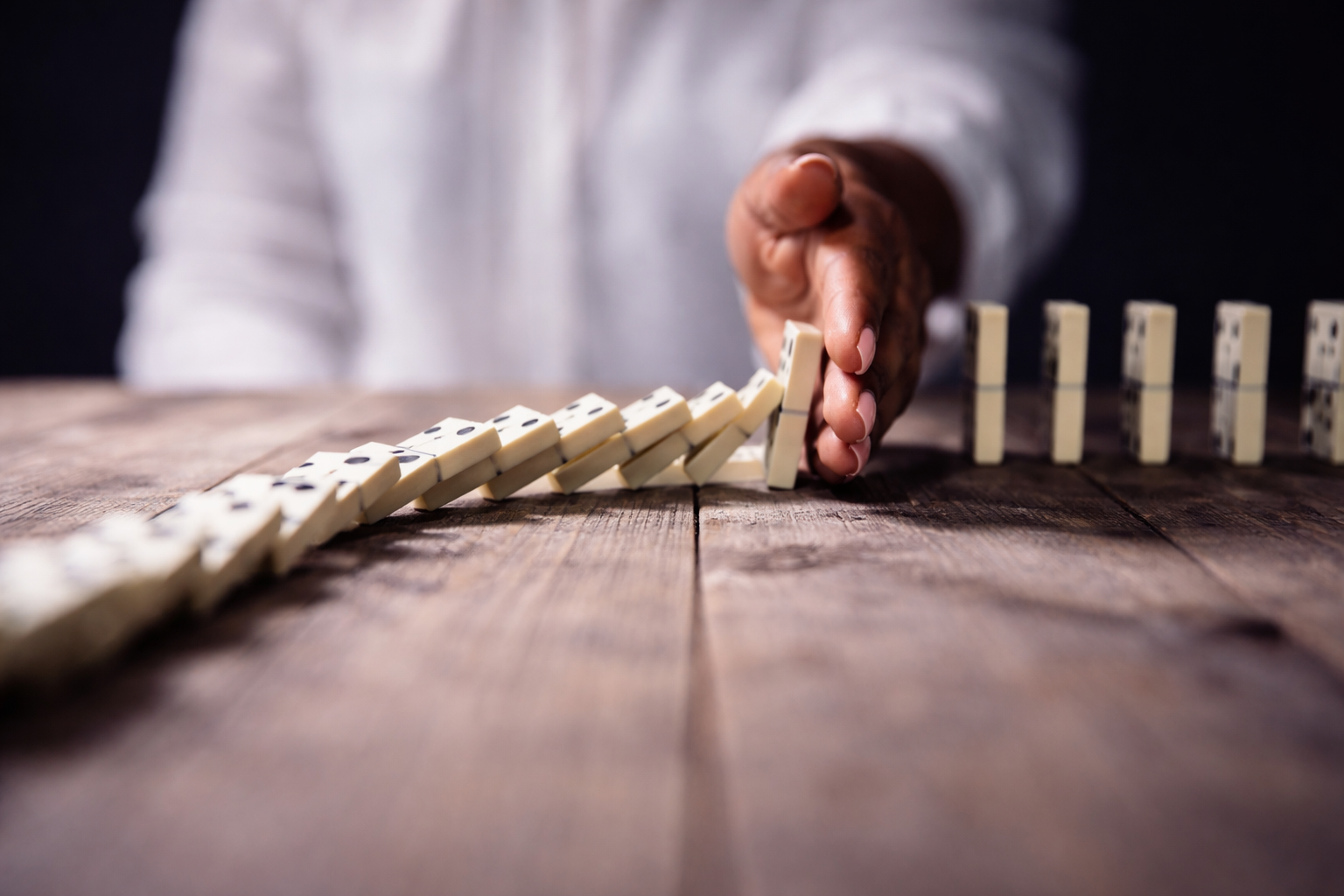 A  hand stopping a line of falling dominoes on a wooden table, symbolising a blocked workflow 