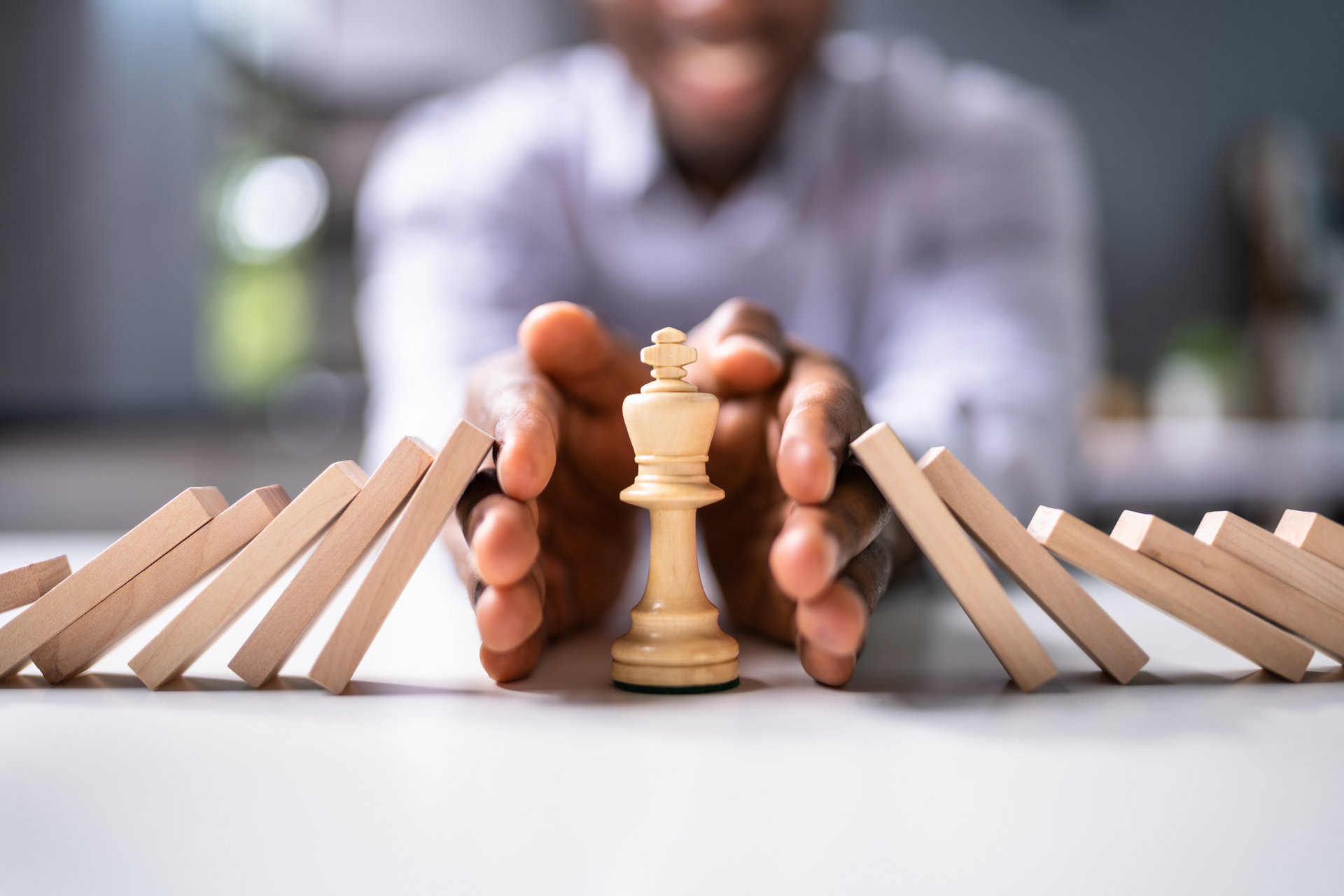 A person blocking falling dominoes with a chess king piece, symbolising strategic decision-making an