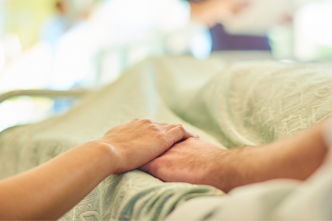 A woman is holding a man 's hand in a hospital bed.