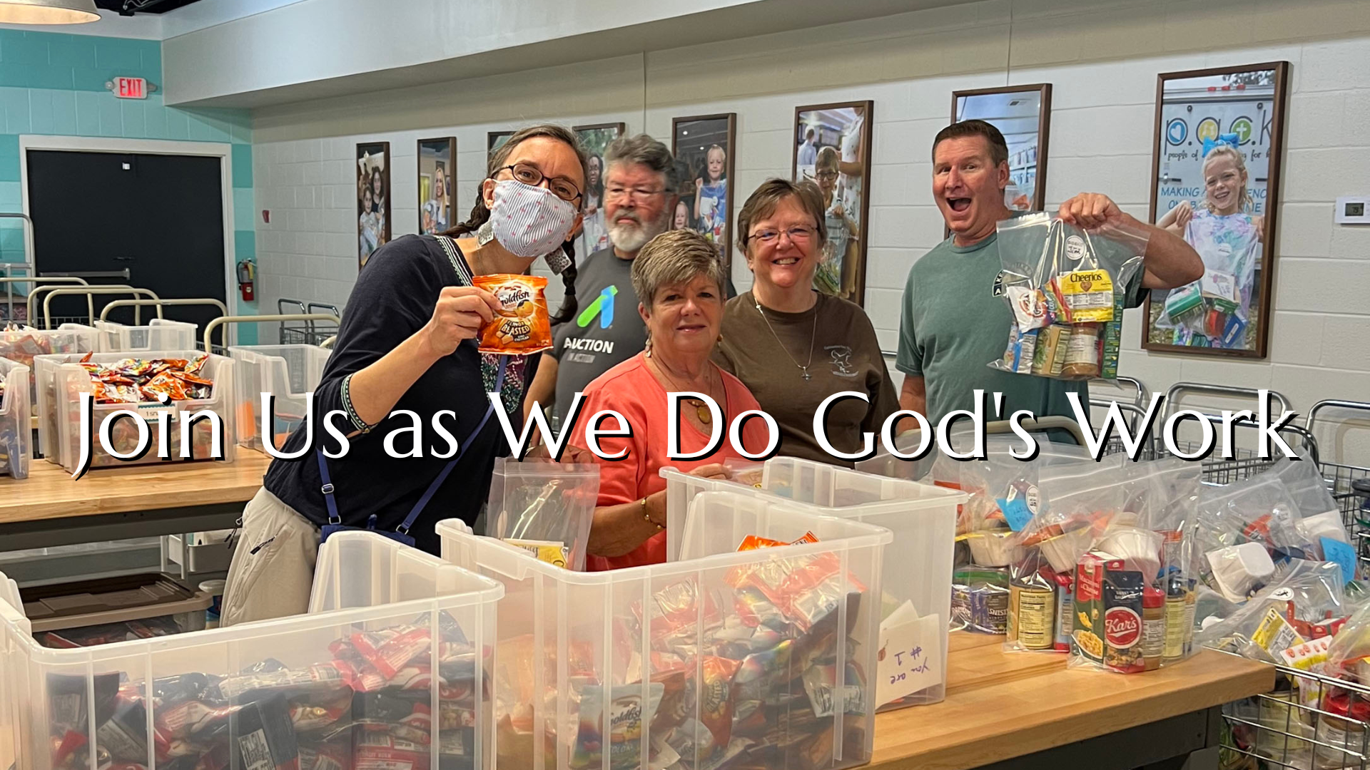 Volunteers packing food items in a kitchen, smiling and holding up items. 