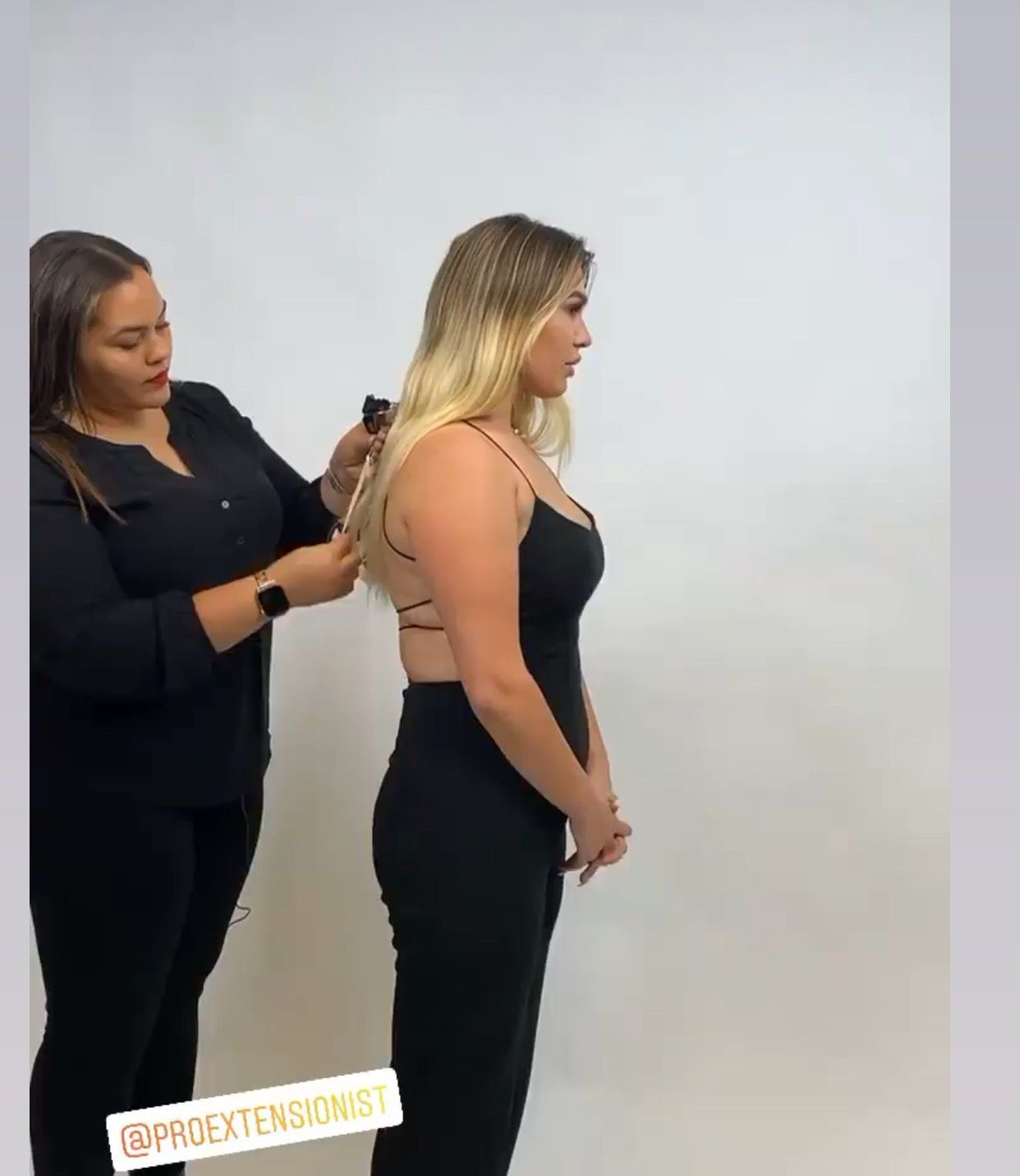 a woman in a black dress is getting her hair done by another woman .