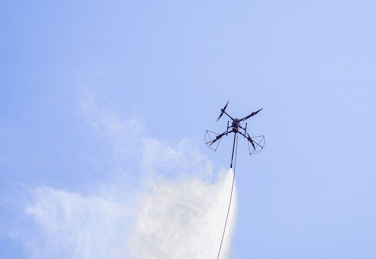 Drone spraying substance in the air against a blue sky.