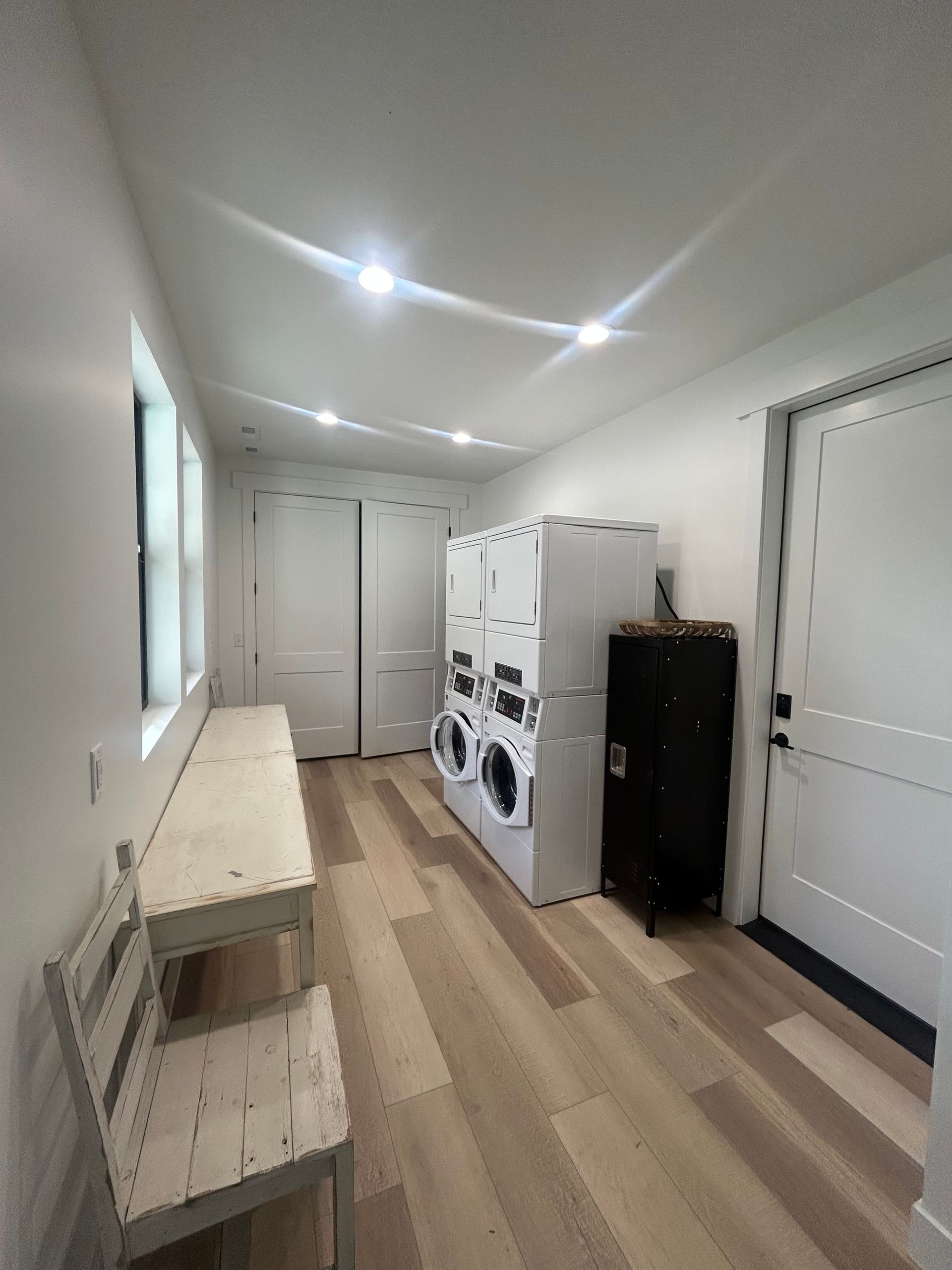 Bright laundry room with stacked washer and dryer, white doors, and light wood floor.