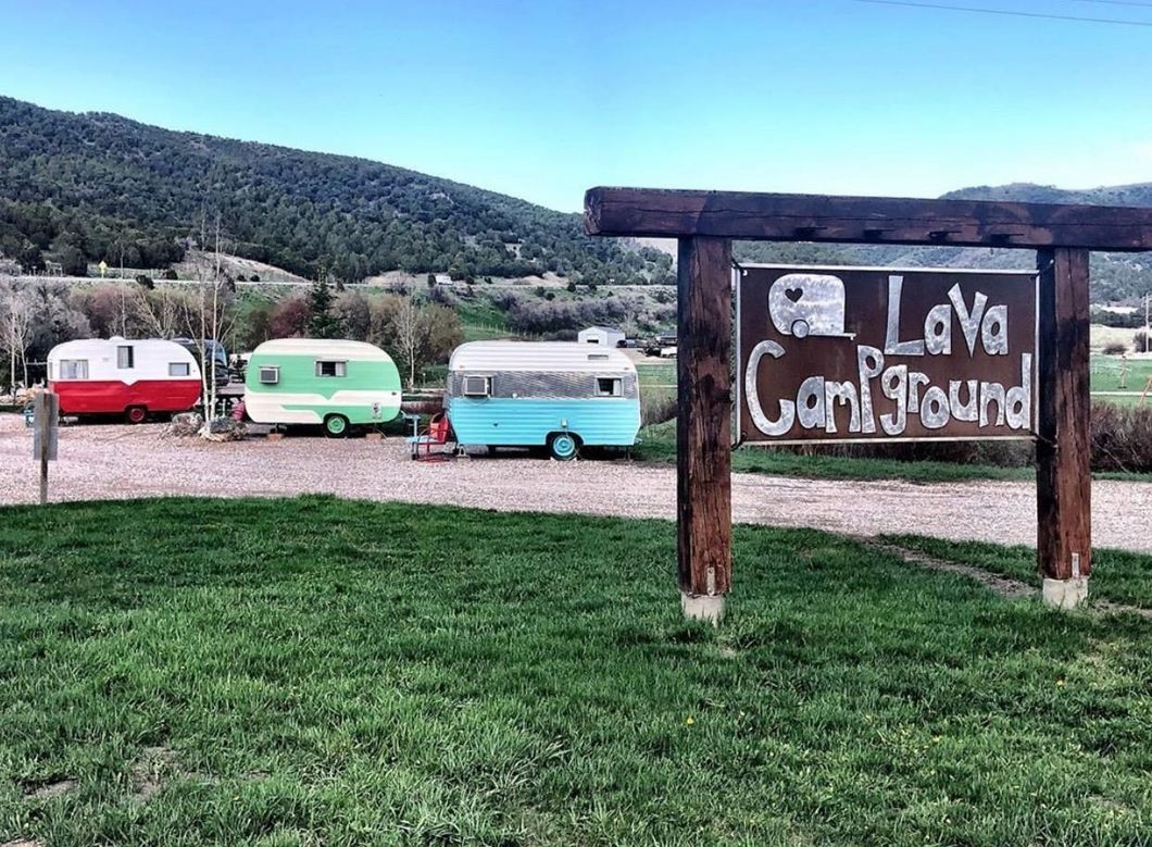 Three colorful campers near a wooden sign reading “Lava Campground” with hills in the background