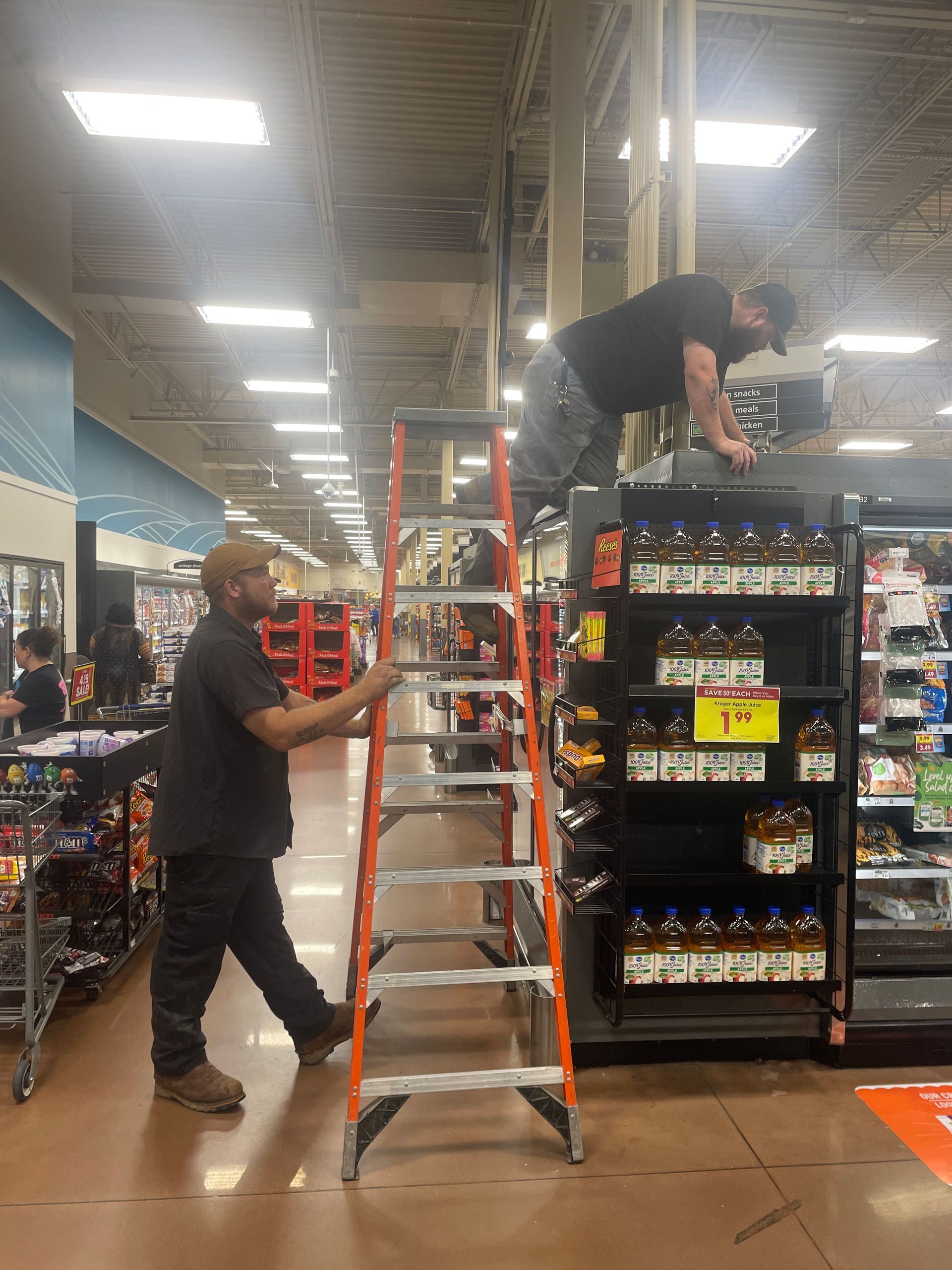 A man is standing on a ladder in a grocery store.