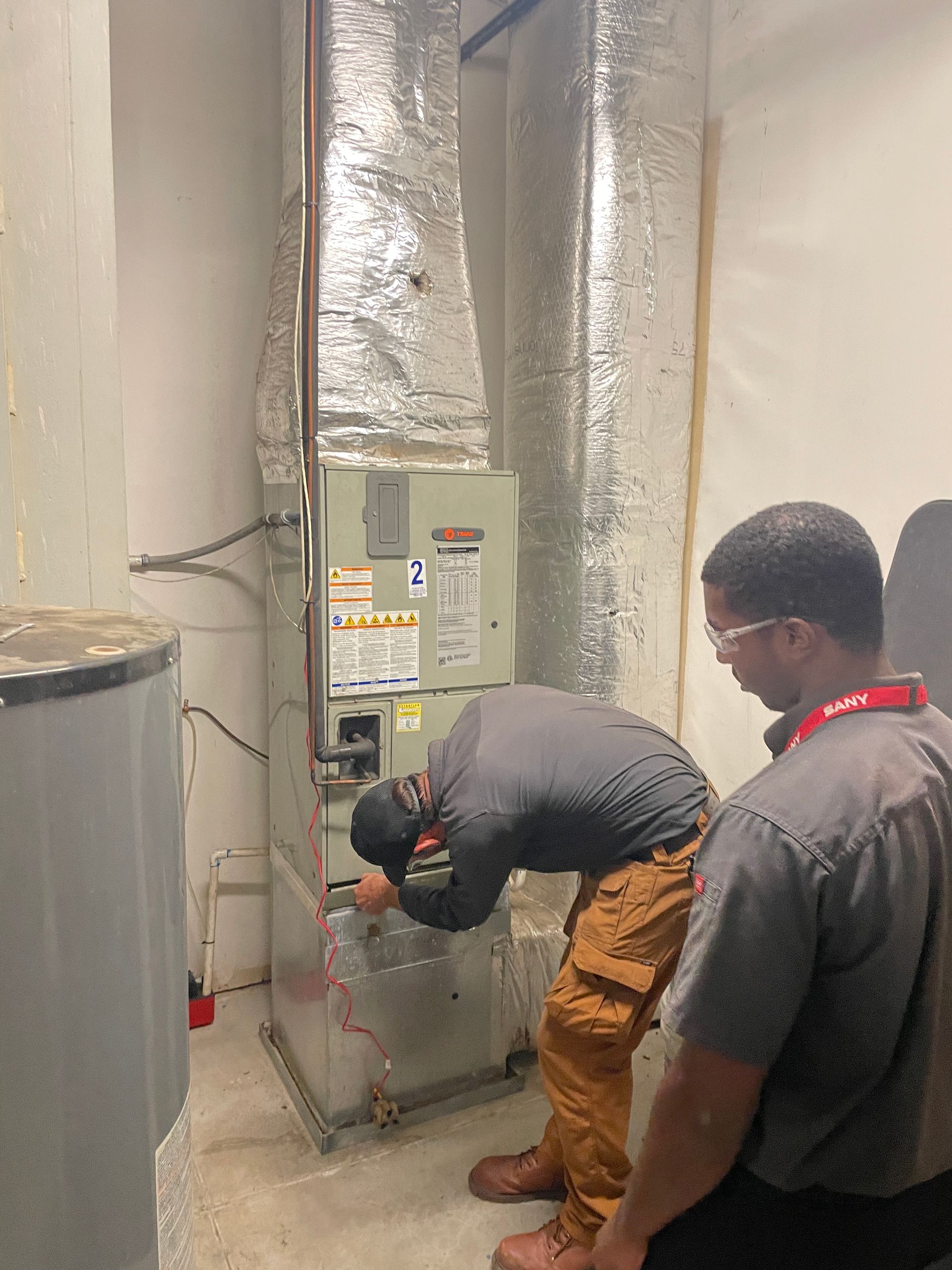 Two men are working on a heating system in a basement.